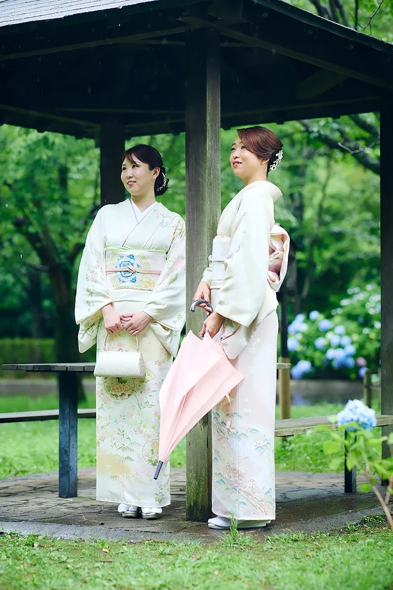 二人の女性が和服を着て、公園の中の休憩所に立っている。