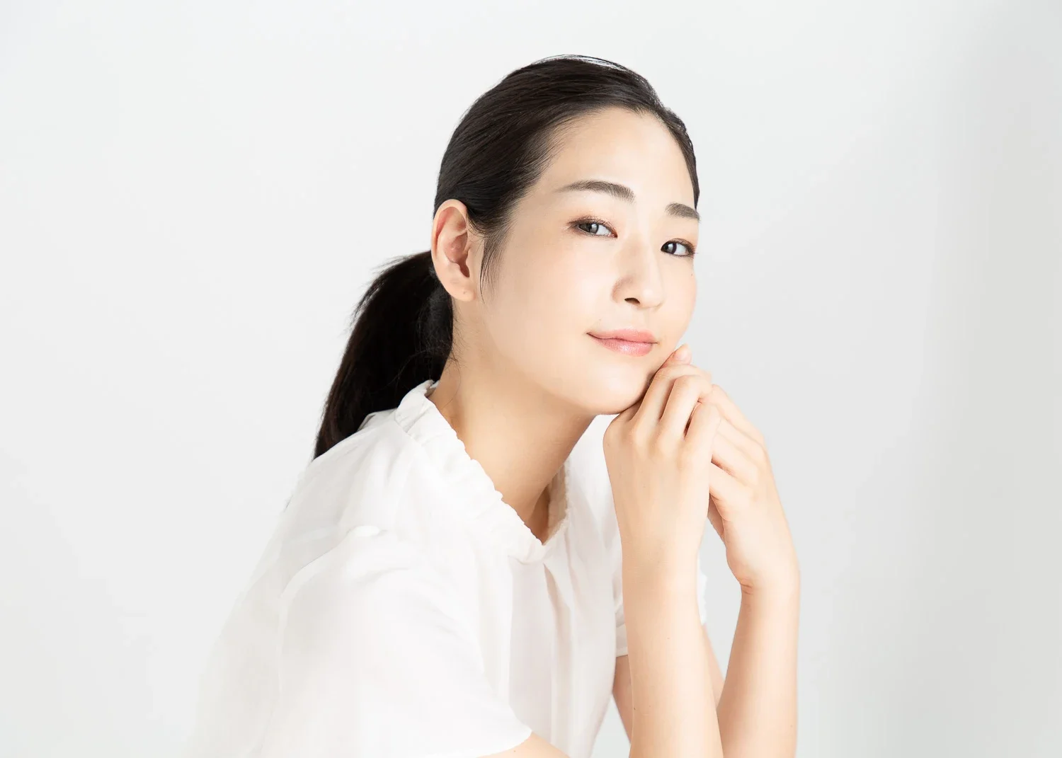 白い服を着た若い女性が微笑みながら顔を手で支えているポートレート