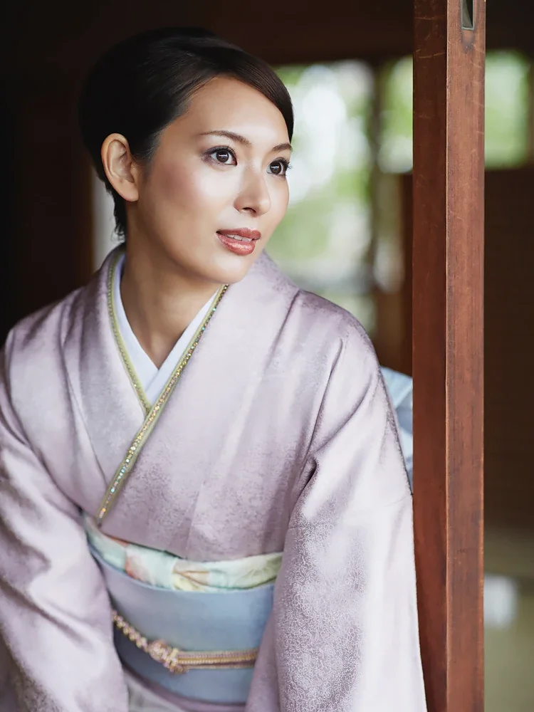 和服を着た女性が木の間に立って外を眺めている。