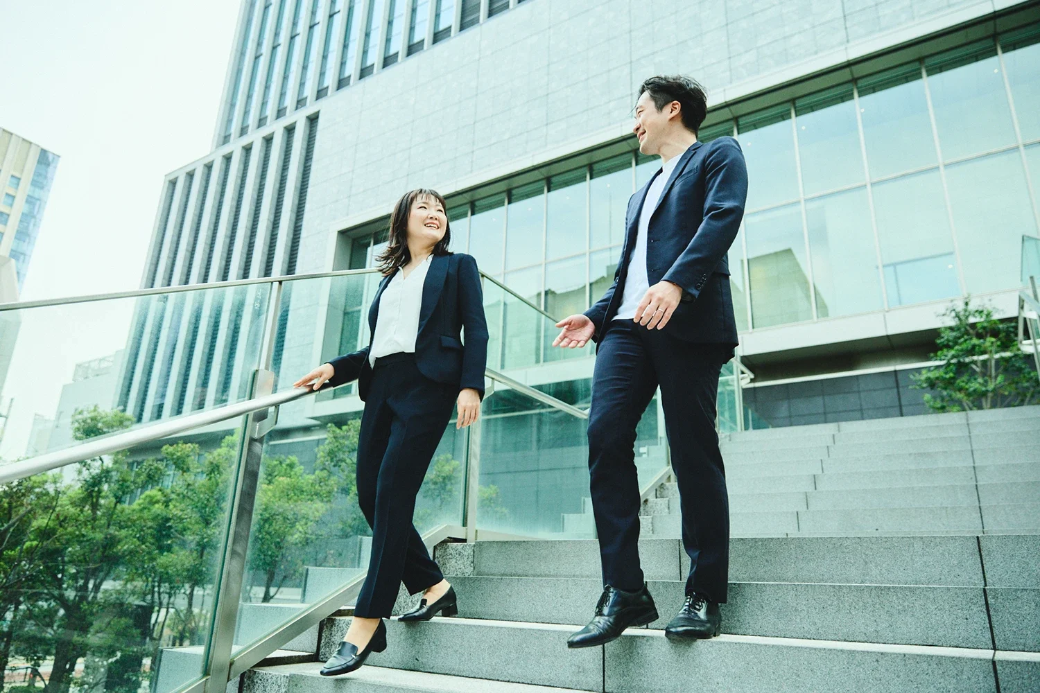 ビジネススーツを着た男性と女性が都市のオフィス街の階段で会話している。