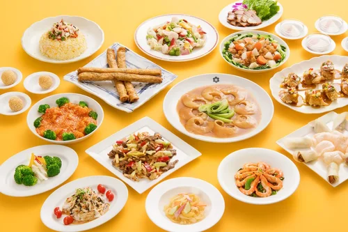 多くの種類の中華料理や前菜が黄色いテーブルに盛り付けられている様子