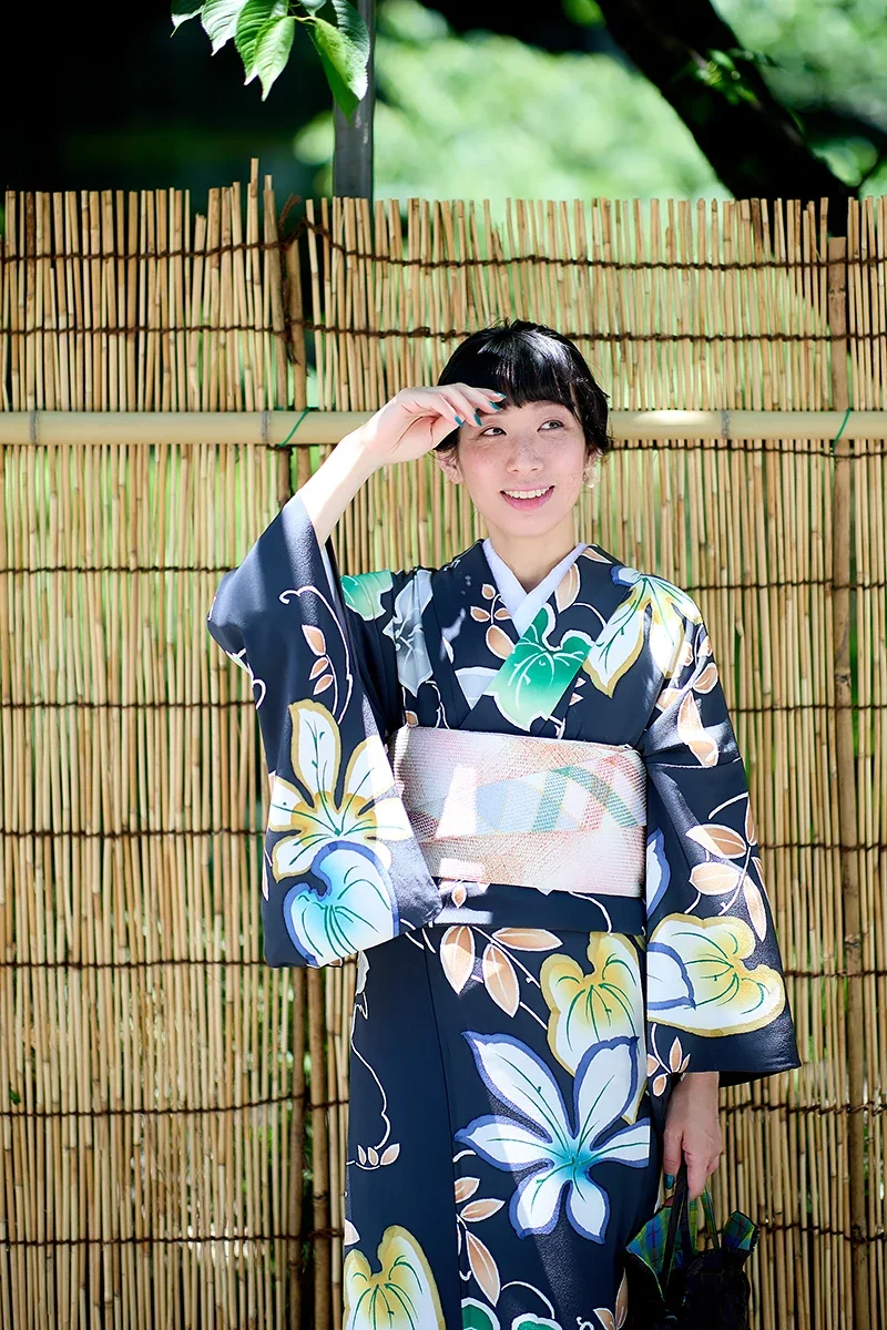 木の垣根の前で浴衣を着た女性が微笑んでいる