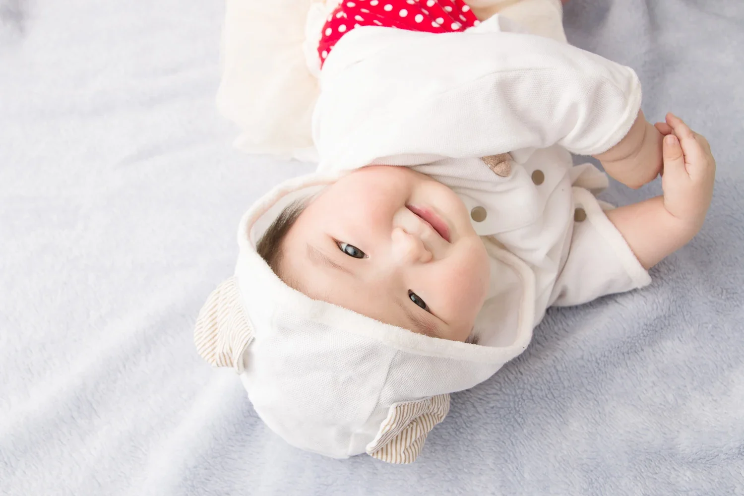 白い帽子をかぶった赤ちゃんが笑って横になっている。