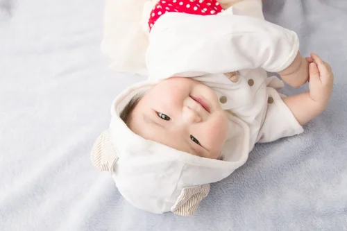 白い帽子をかぶった赤ちゃんが笑って横になっている