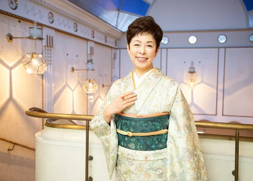 着物を着た笑顔の中年女性が屋内の背景の前でポーズをとっている画像
