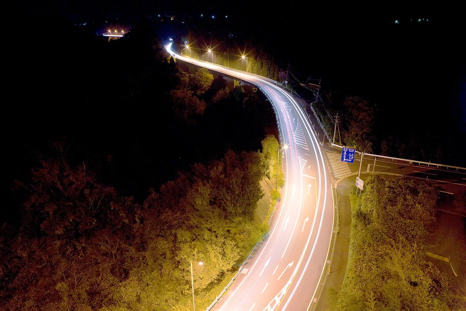 夜の静寂を切り裂く光の軌跡。長時間露光で捉えたドラマチックな高森の峠道と、躍動する都市の動脈イメージ（江藤耕治 撮影）