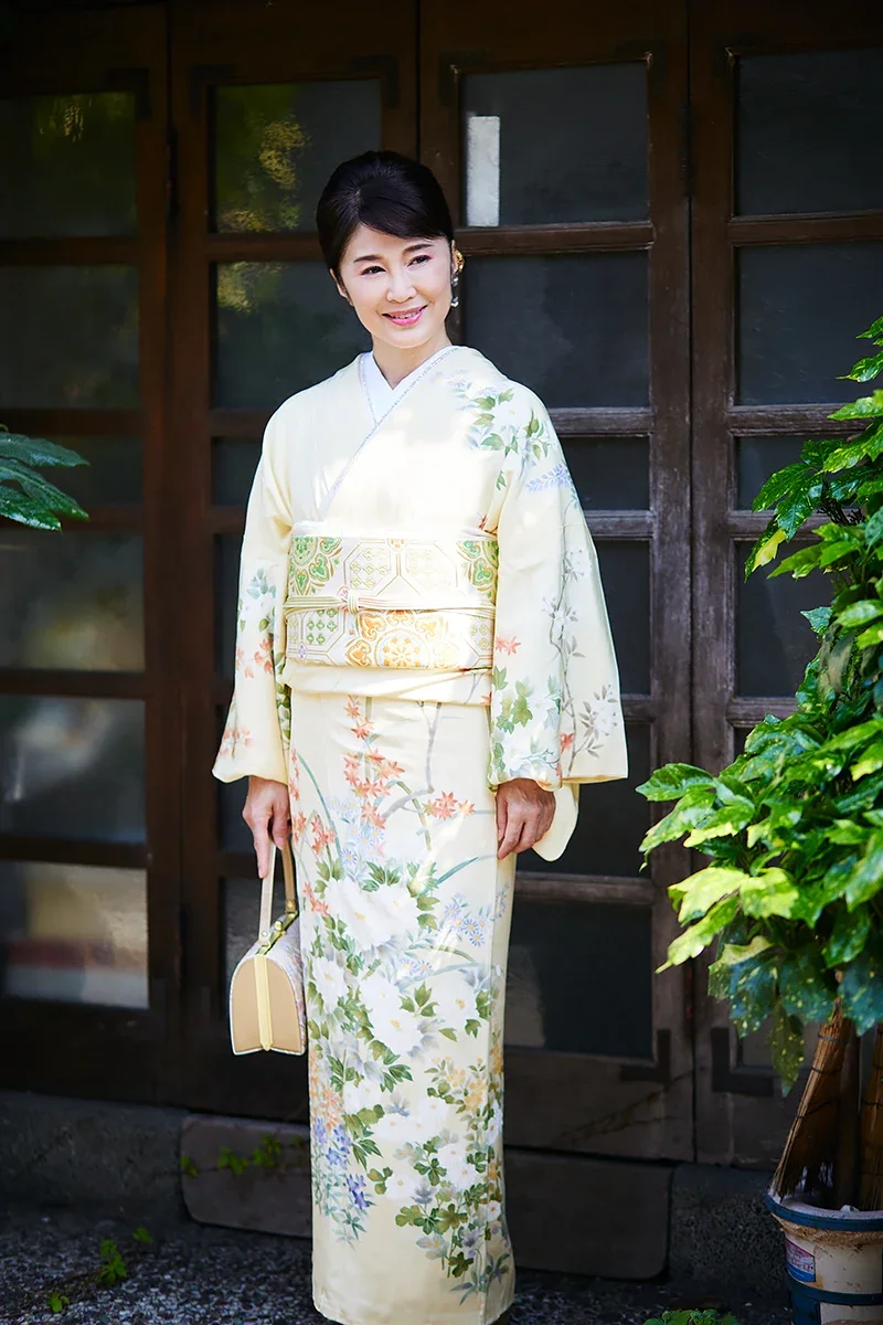 着物を着た女性が和風の家の前で微笑んでいる