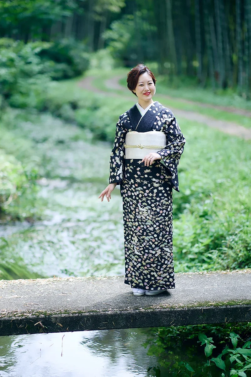 林の中の小さな橋の上に立つ女性。和服を着ている。