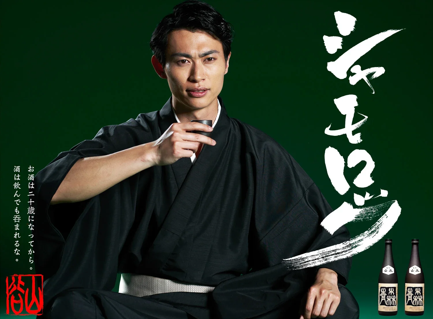黒い着物を着た男性が、緑の背景の前でお猪口を持っている。右側に日本語のキャッチコピーと二本の酒の瓶と、そのラベル。