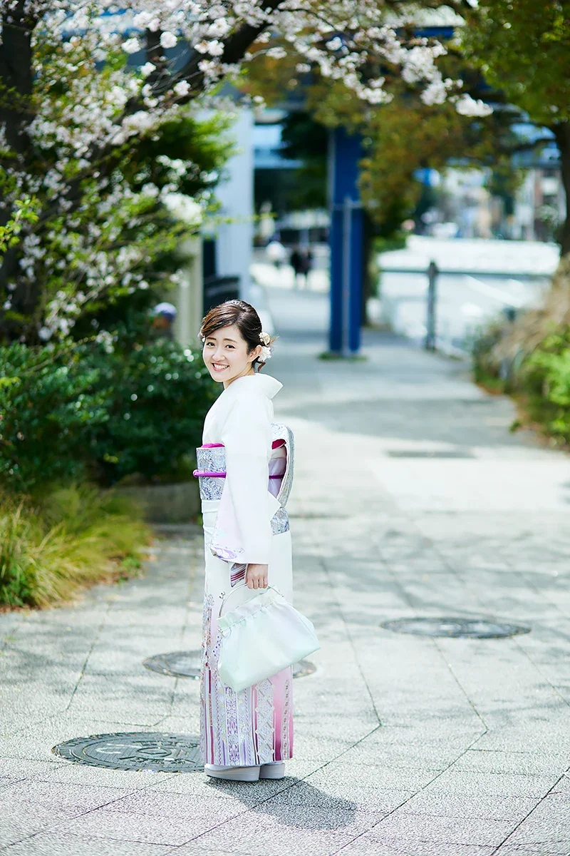 着物を着た女性が笑顔で歩いている。背景は桜の木や街並み。