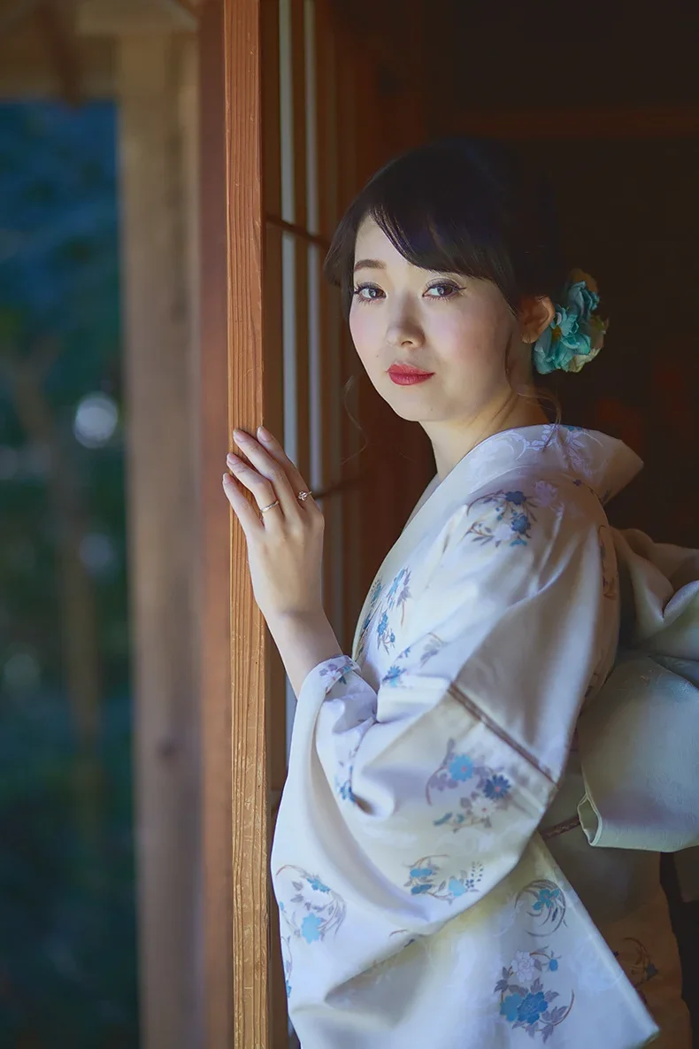 和服を着た女性が木の窓枠に手をつきながら外を見ている