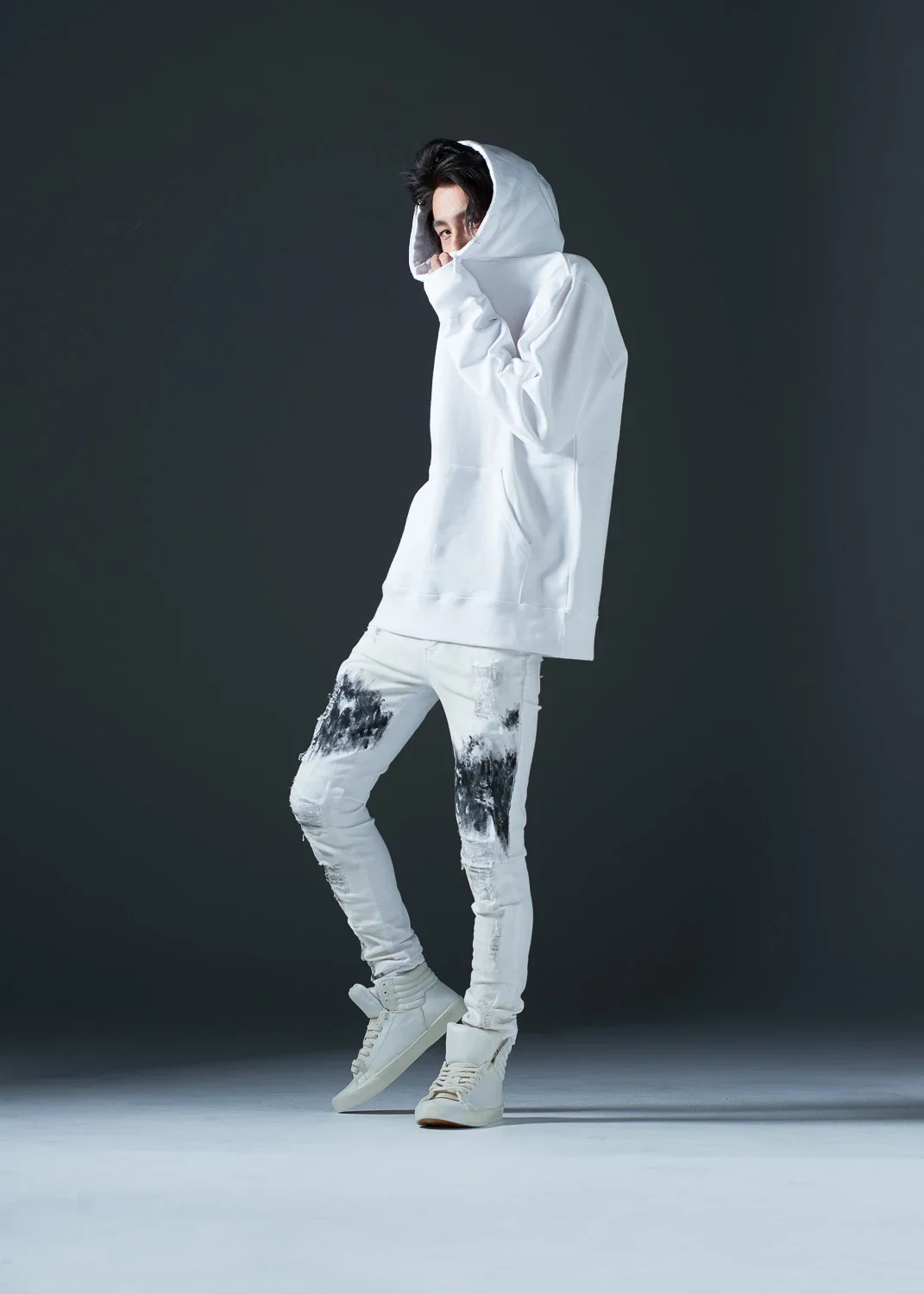 白いパーカーとスニーカーを履いた若い男性がポーズをとっている写真