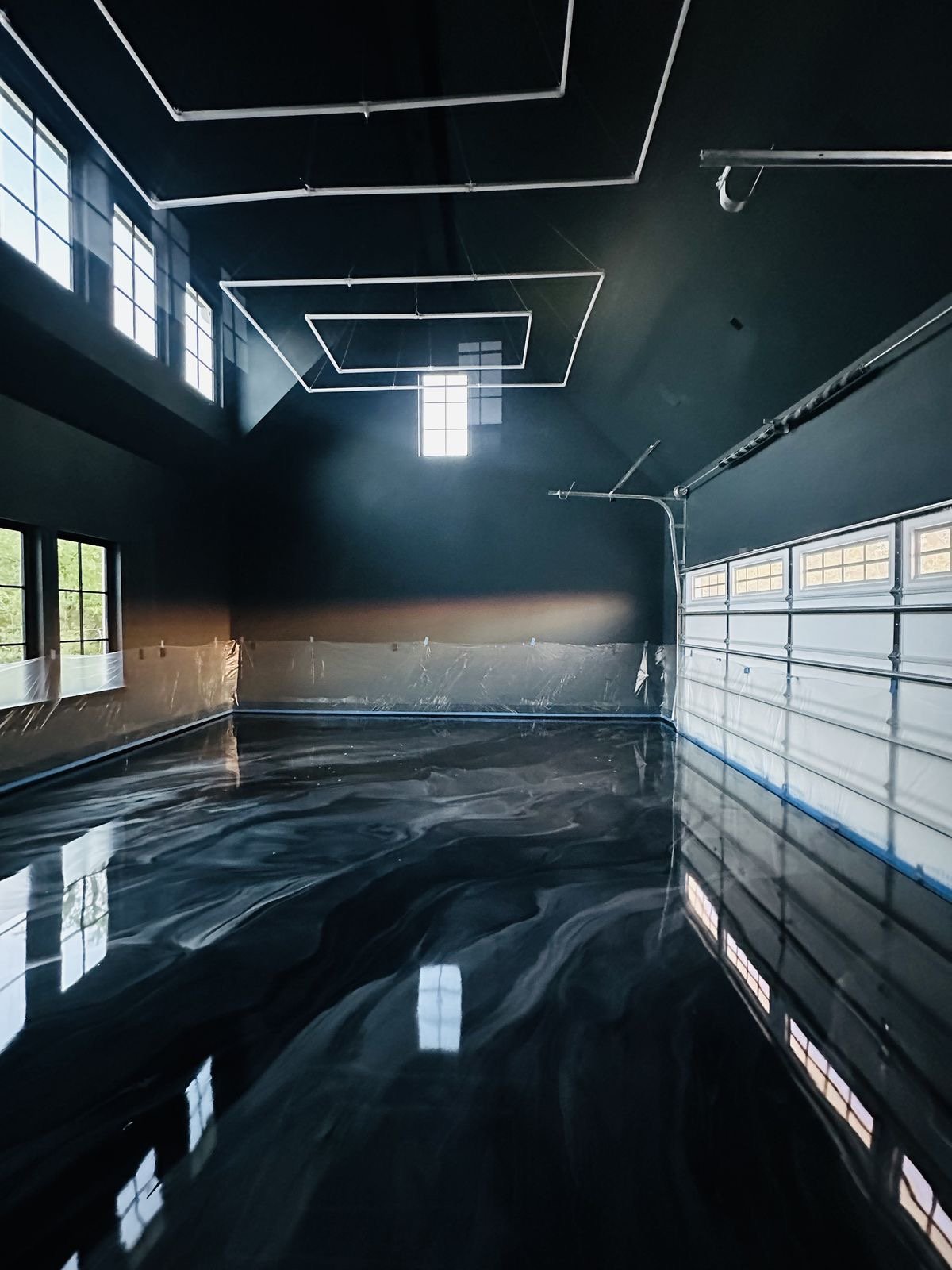 Époxy métallique sombre, avec lumière naturelle entrant par de grandes fenêtres et un plafond haut avec des luminaires géométriques suspendus.