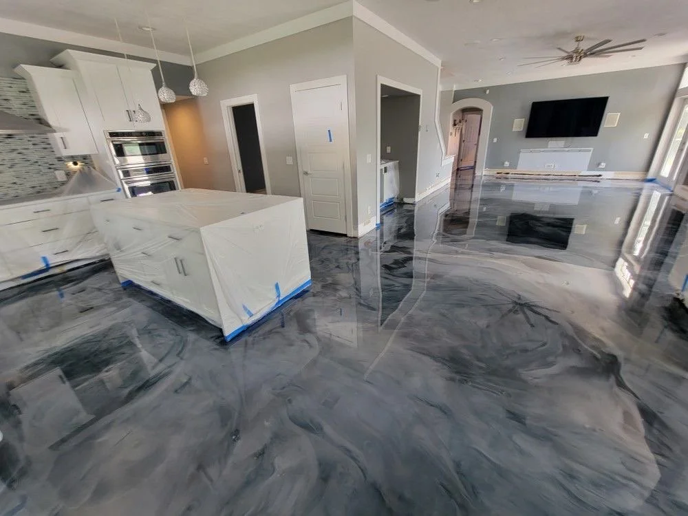 Salon contemporain avec plancher en époxy métallique gris, cuisine avec îlot blanc, et murs gris clair, avec télévision murale et fenêtre grande.