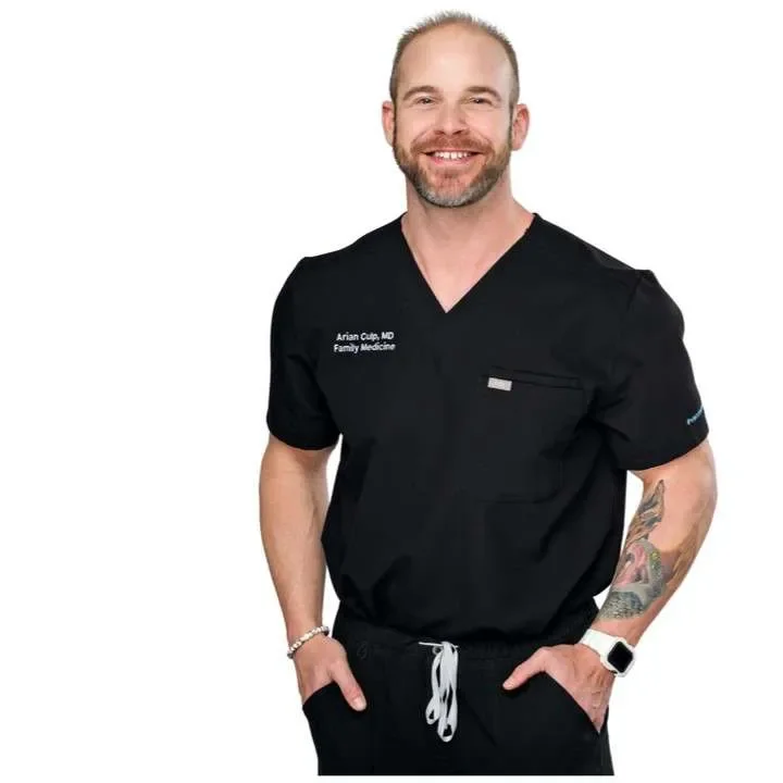 Half-length portrait photo of Dr. Arian Culp MD, wearing black scrubs with a name tag, smiling, and standing against a white background.
