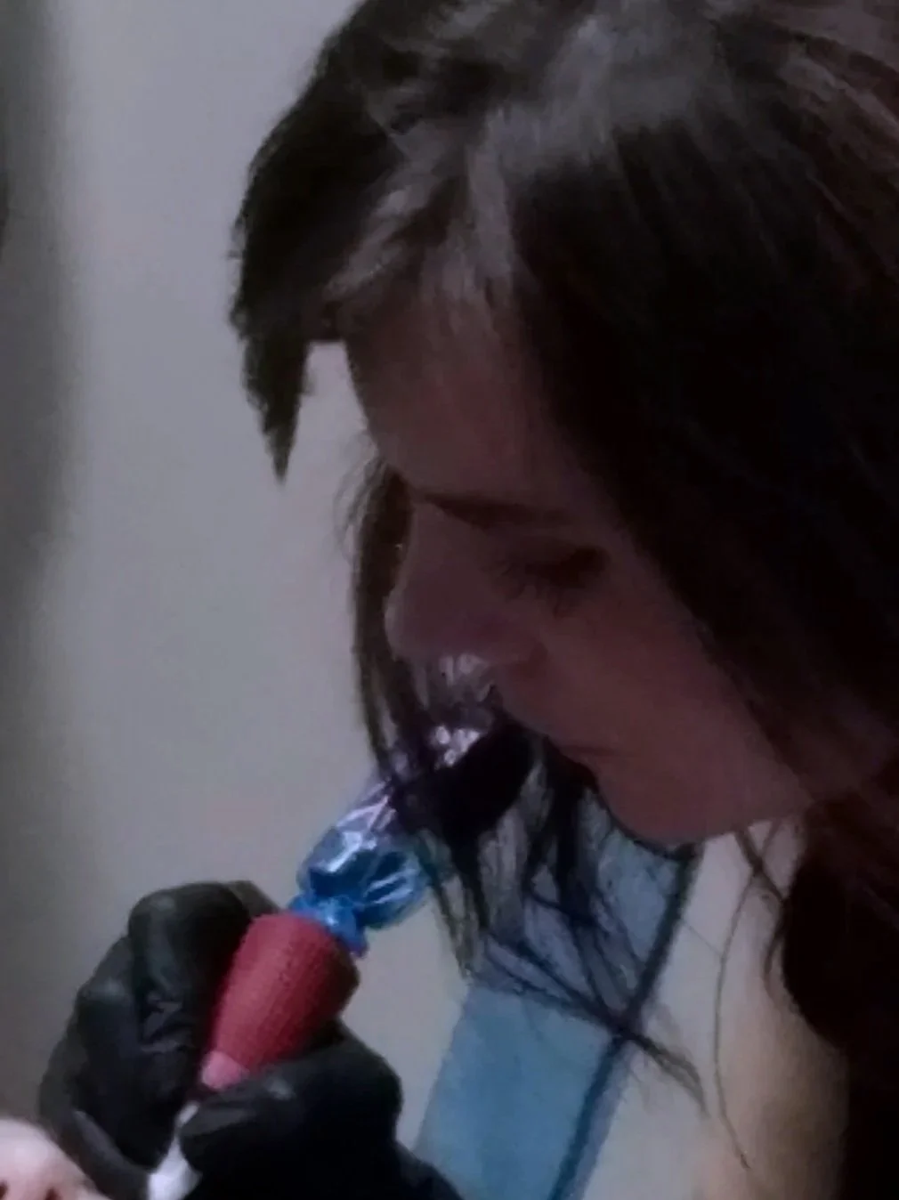 A close-up photo of Liz Cook Tattoo leaning in to demonstrate a tattoo during a class, wearing a black glove on her right hand and holding a Bishop Fantom rotary tattoo machine.