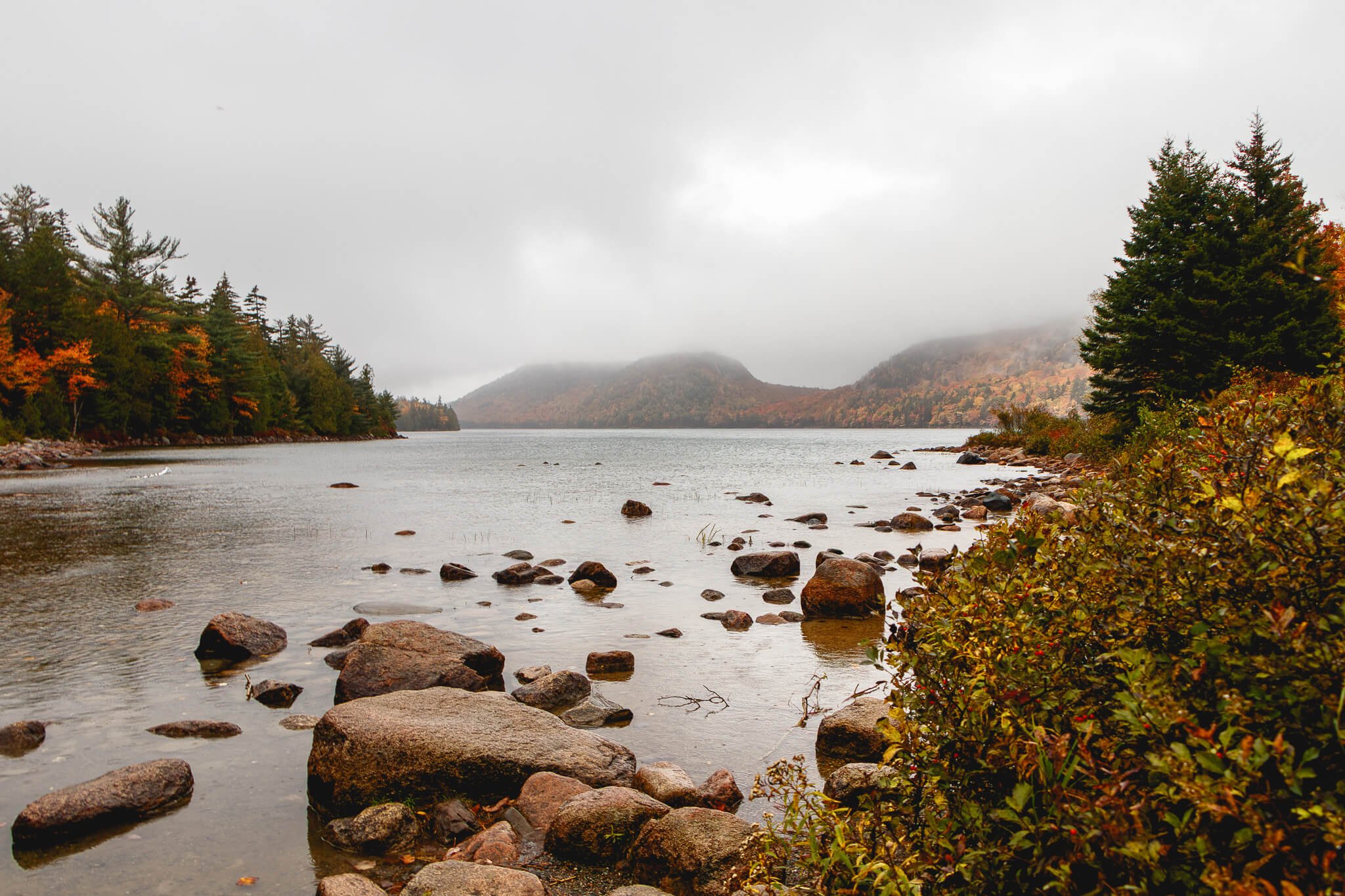 Rocky shoreline of Jordan Pond in Maine with fog over the Bubbles mountains