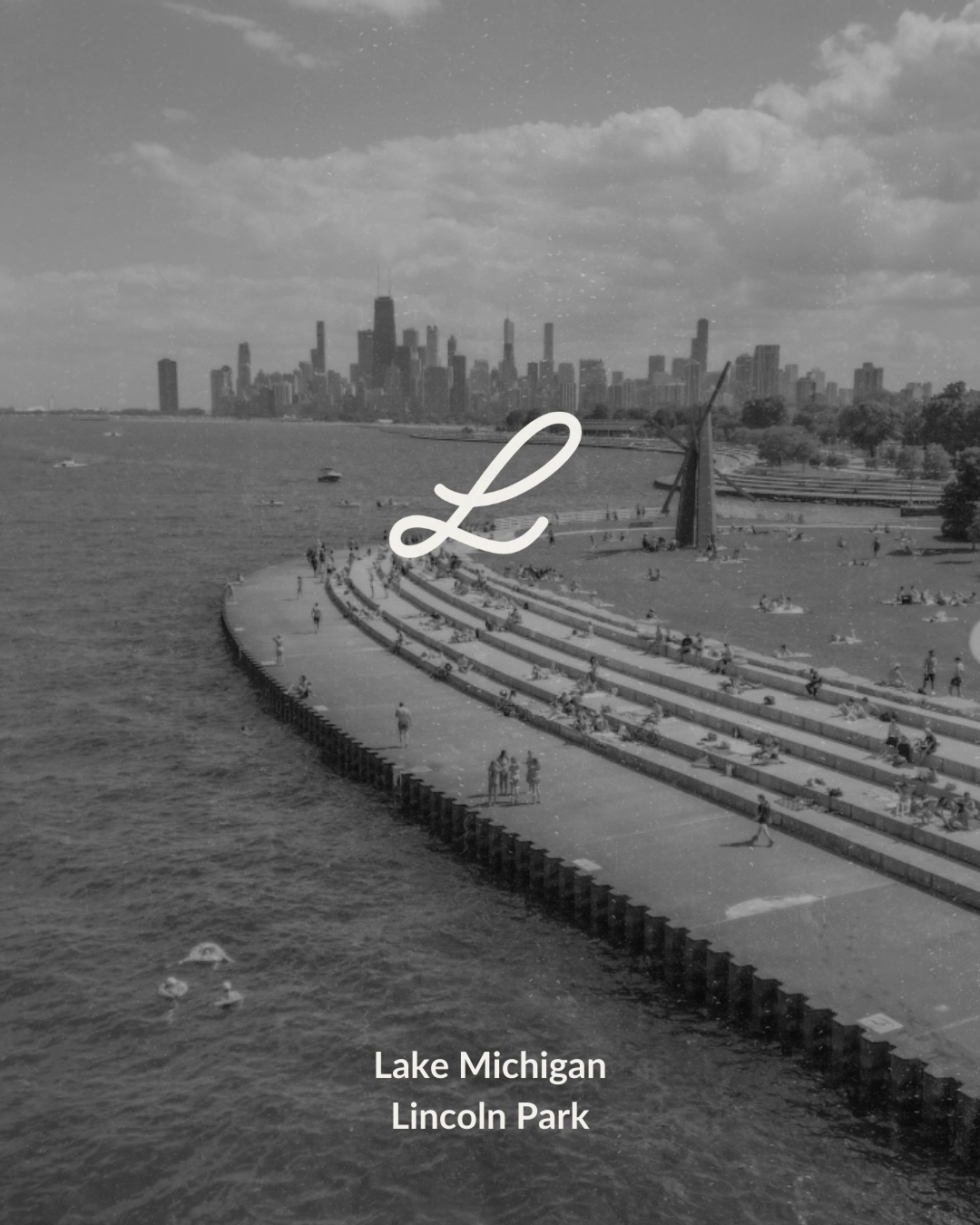 Black and white photo of Lake Michigan and Chicago skyline as seen from Lincoln Park, with people relaxing on the shoreline and the city skyline in the background.