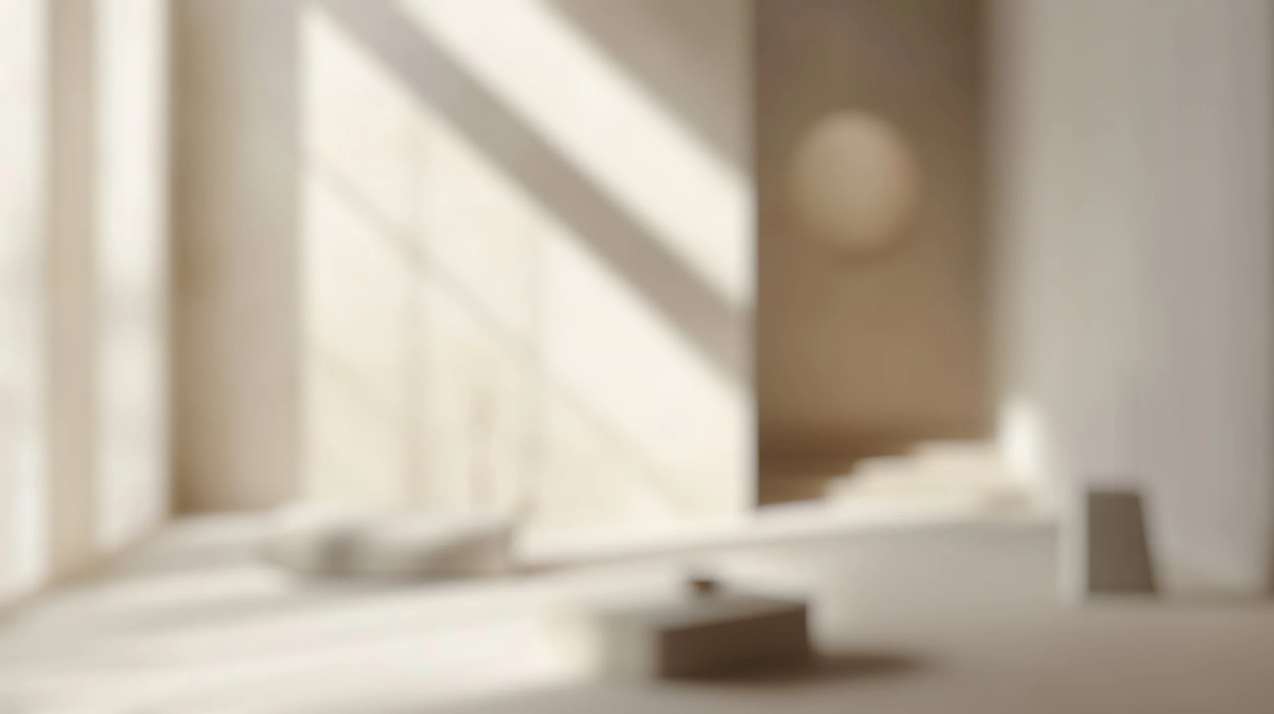 A blurred image of a window with sunlight casting shadows on a white wall inside a room.