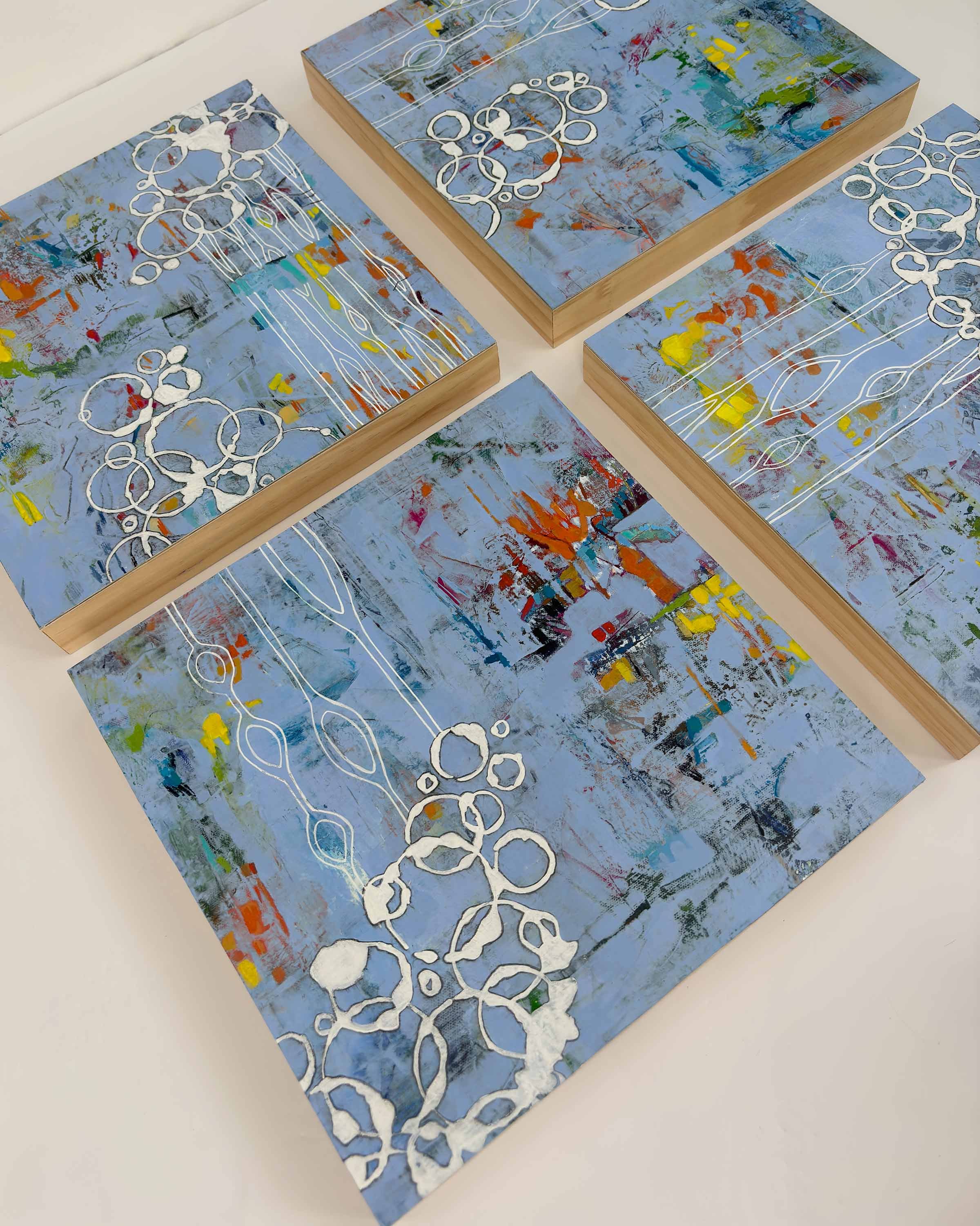 Four-panel abstract painting Hidden Tides by Calie Durant shown from above, featuring soft blue tones, layered textures, and bold accents of yellow, orange, and red with white linear details.