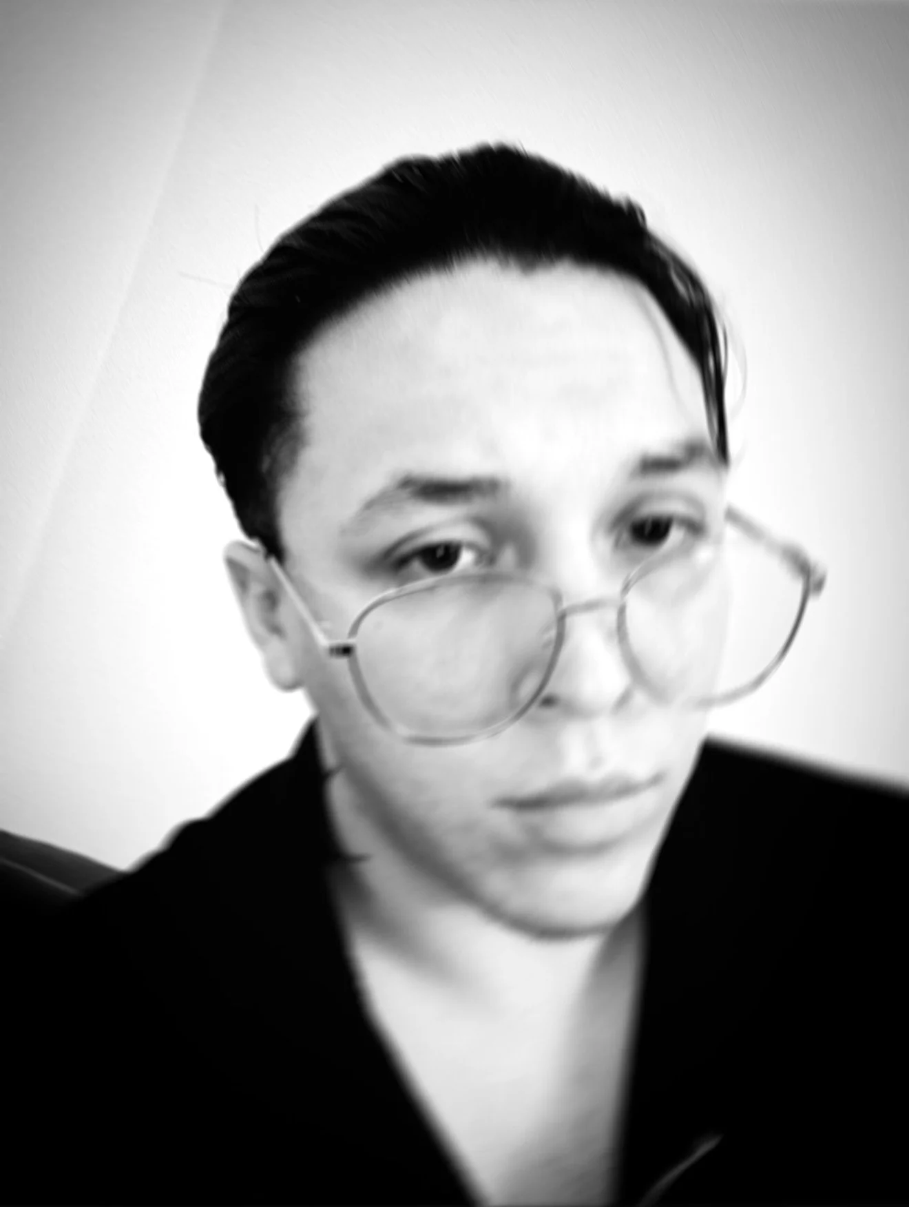 Black and white close-up portrait of a person with short dark hair, round glasses, and a neutral expression, looking slightly to the side.