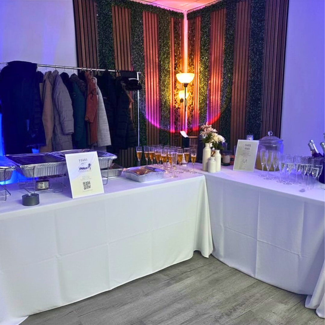 A buffet table set for a celebration with food, drinks, and flowers, with a coat rack in the background.