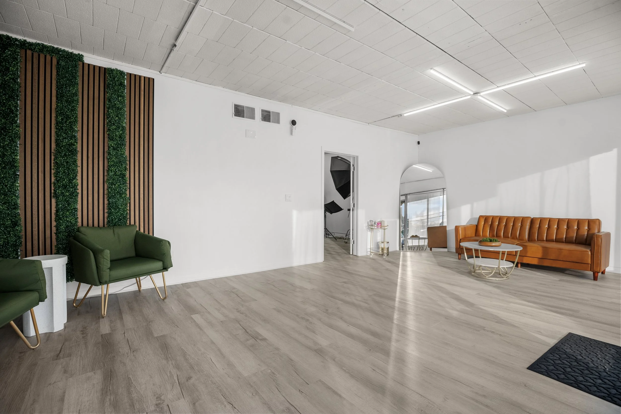 A spacious, modern living room with white walls, light wood flooring, green and orange sofas, and minimal decor.