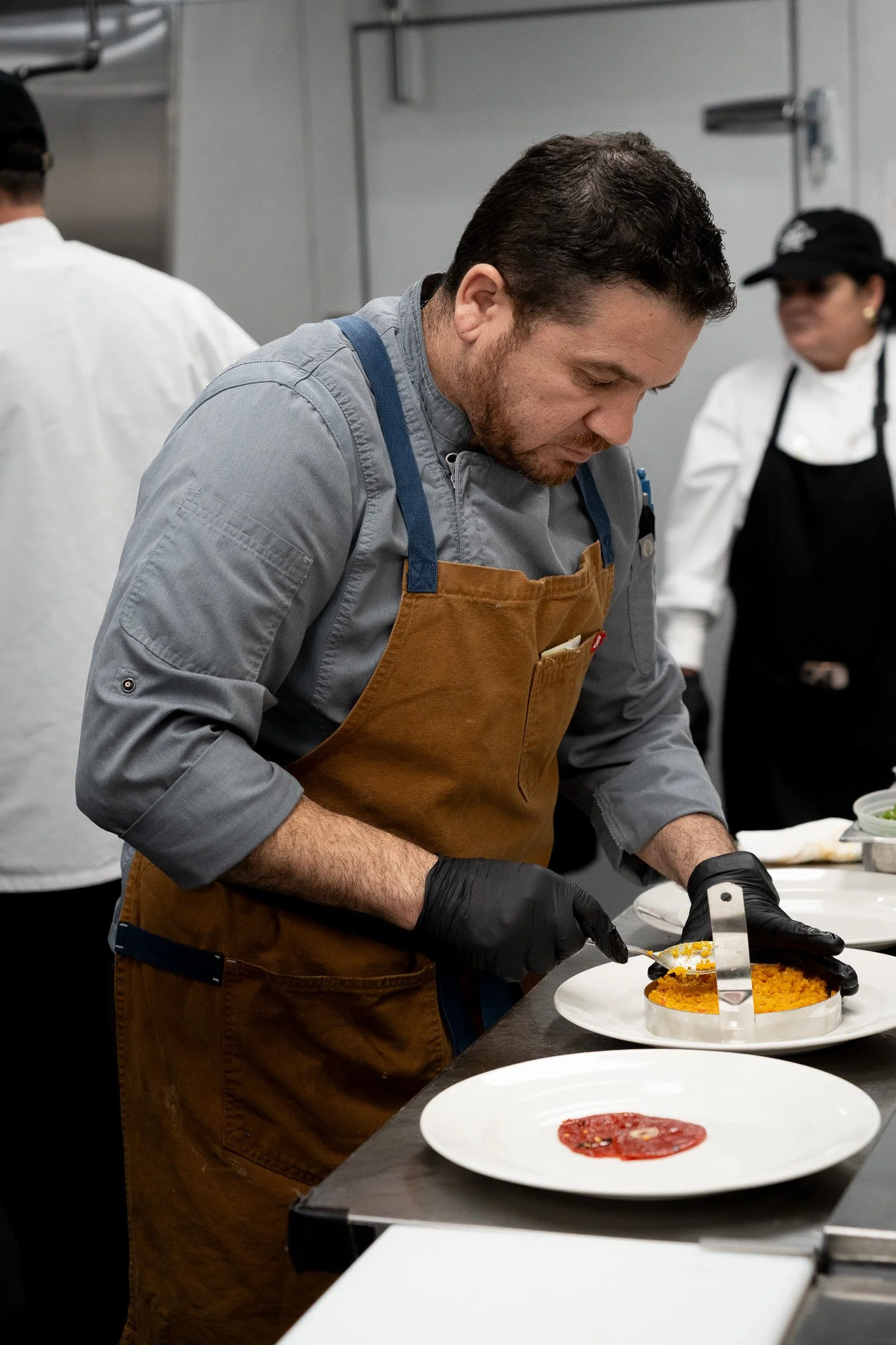 A chef with black gloves assembling a dish in a professional kitchen.