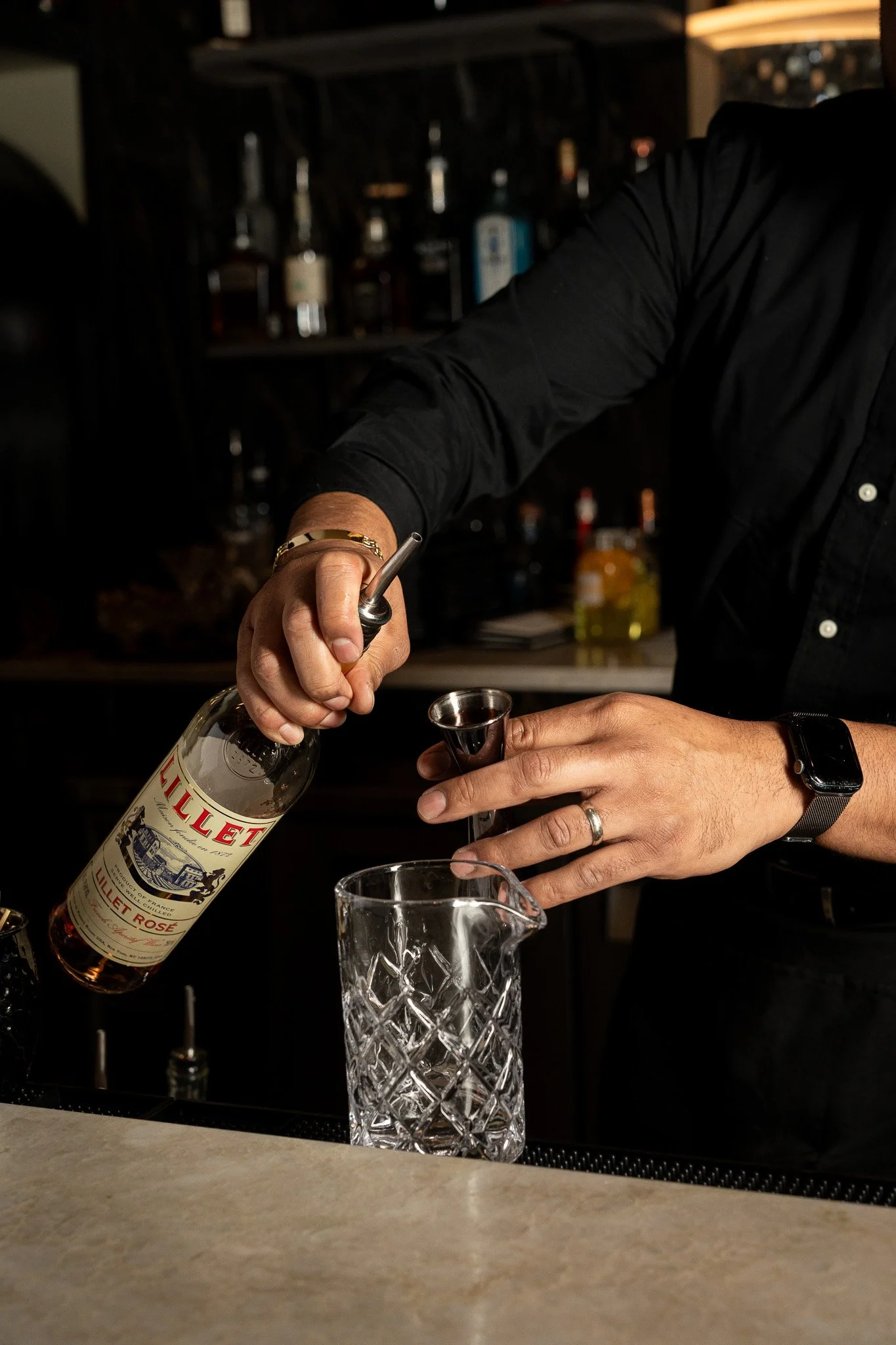 Person pouring Rosé wine from a bottle into a jigger at a bar.
