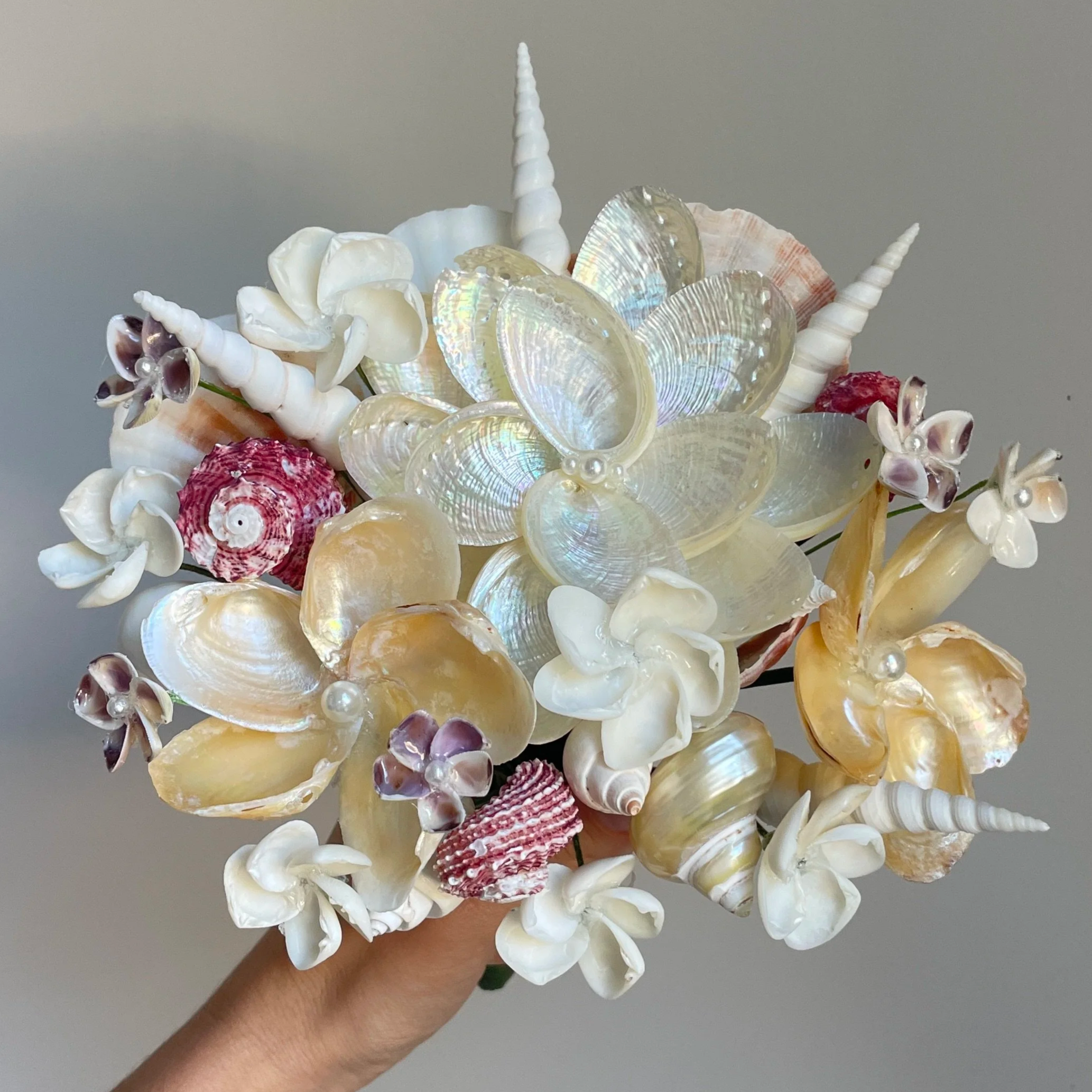 Close-up of a bouquet of seashells, pearls, and starfish being held in a person's hand.
