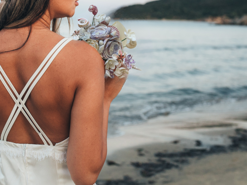 Woman in a white dress holding a bouquet of seashells on a beach