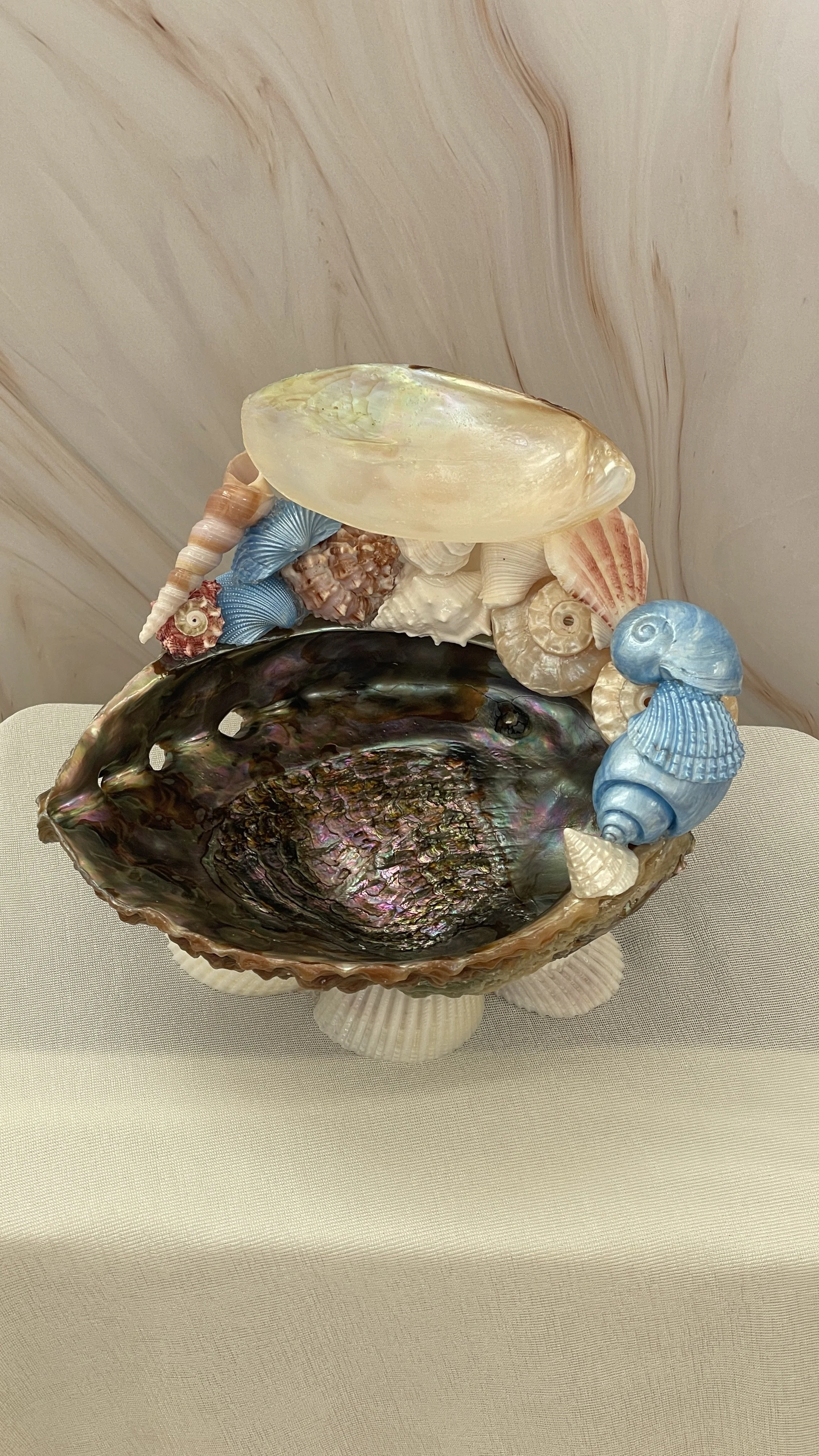 A decorative seashell display with various seashells and coral arranged around a large, iridescent shell to form a bowl.