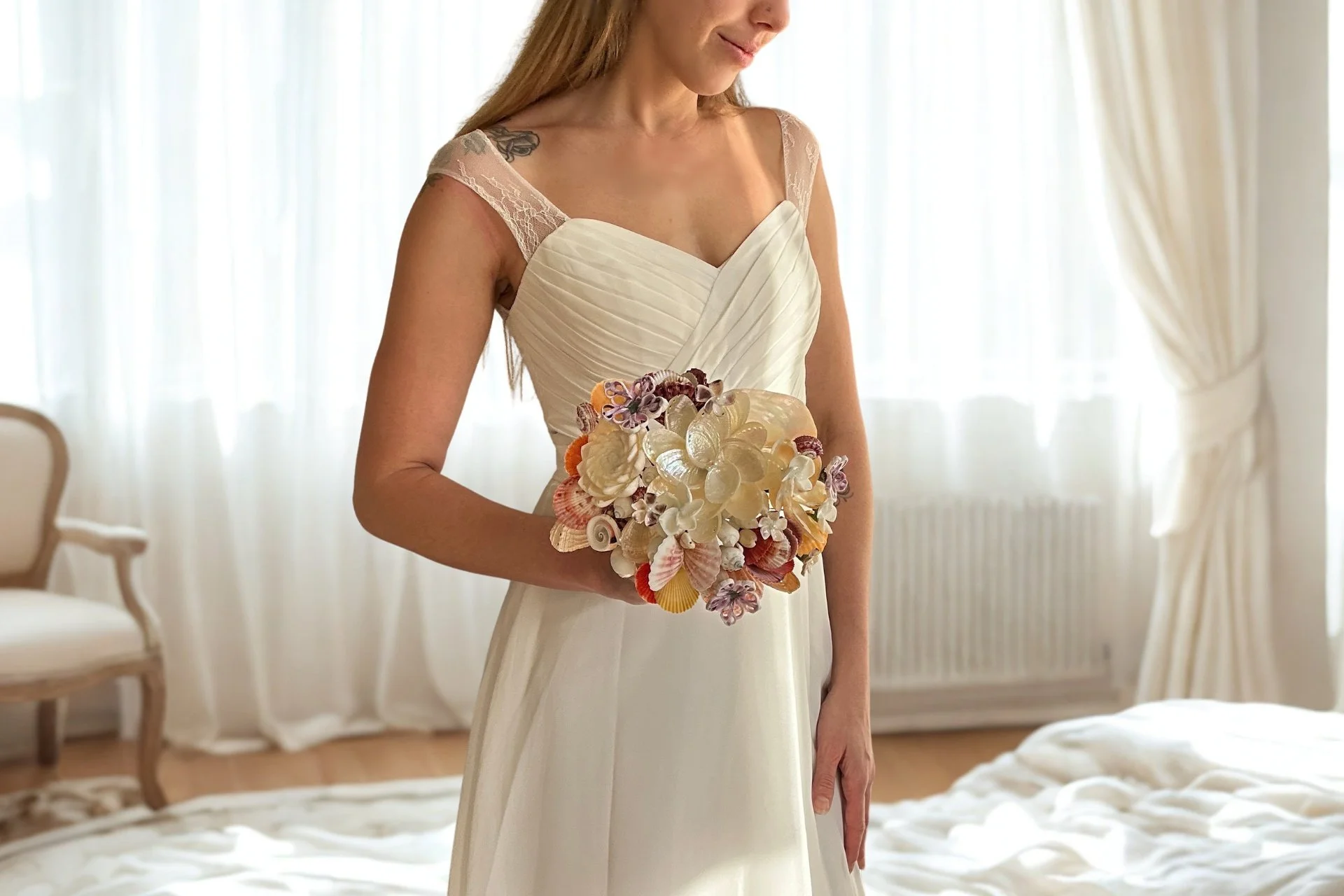 A woman in a white wedding dress holding a bouquet of seashells, standing in a bright room with light colored curtains.