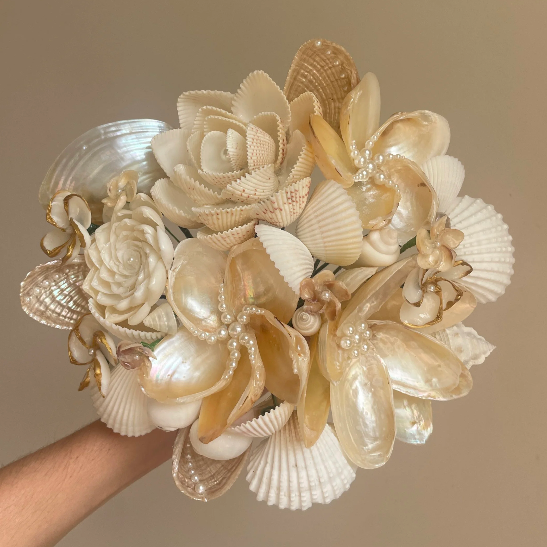 Hand holding a bouquet of seashells, pearls, and coral, arranged as a floral display.