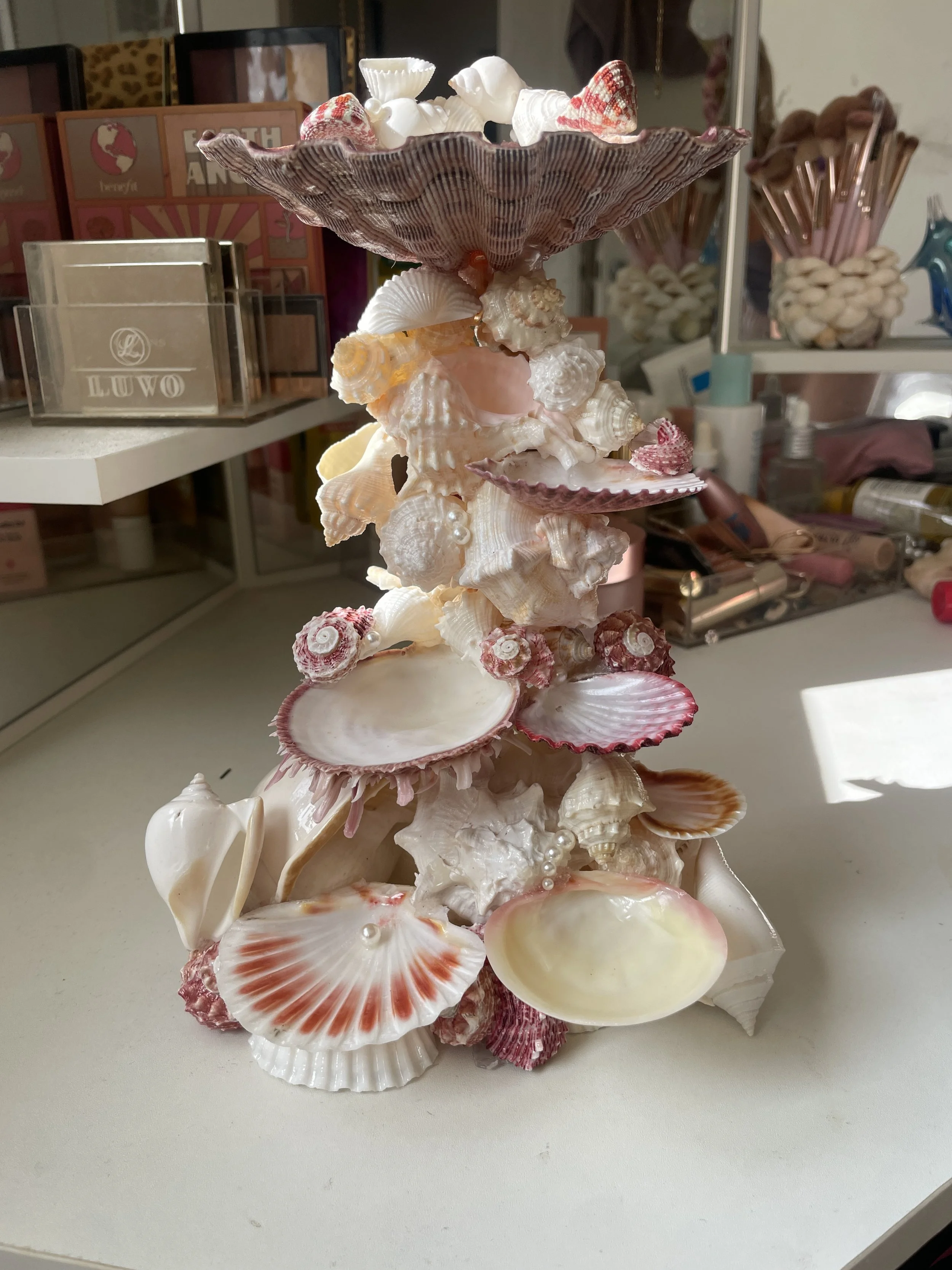 A decorative structure made of various seashells arranged in a tower, with a large purple scallop shell at the top and smaller shells cascading down.