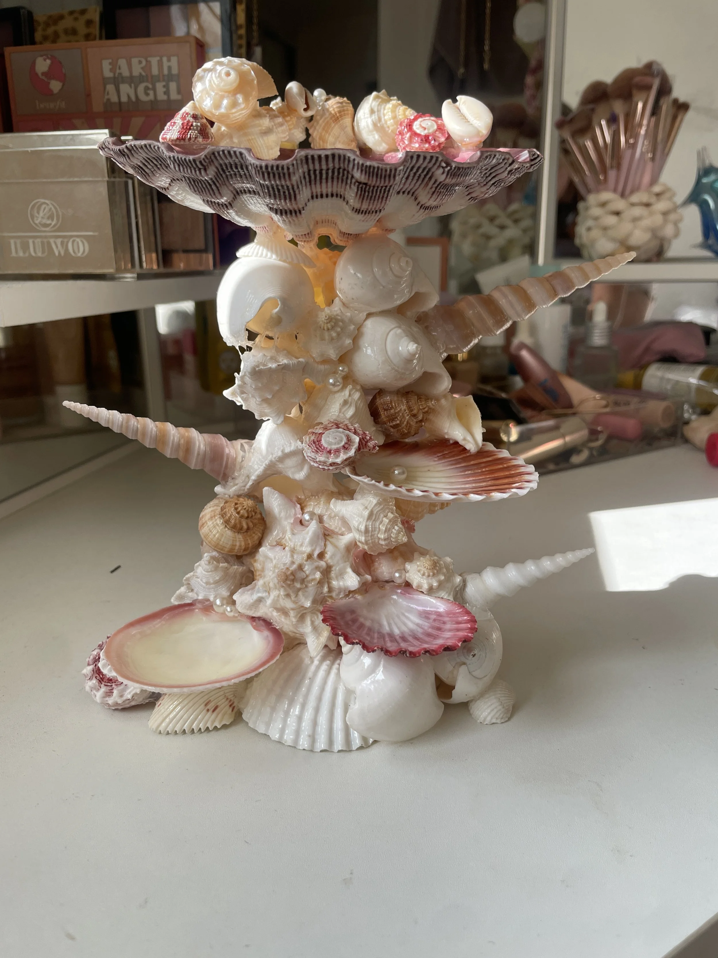A decorative sculpture made of various seashells arranged in a tiered, possibly spiral pattern, on a white surface.