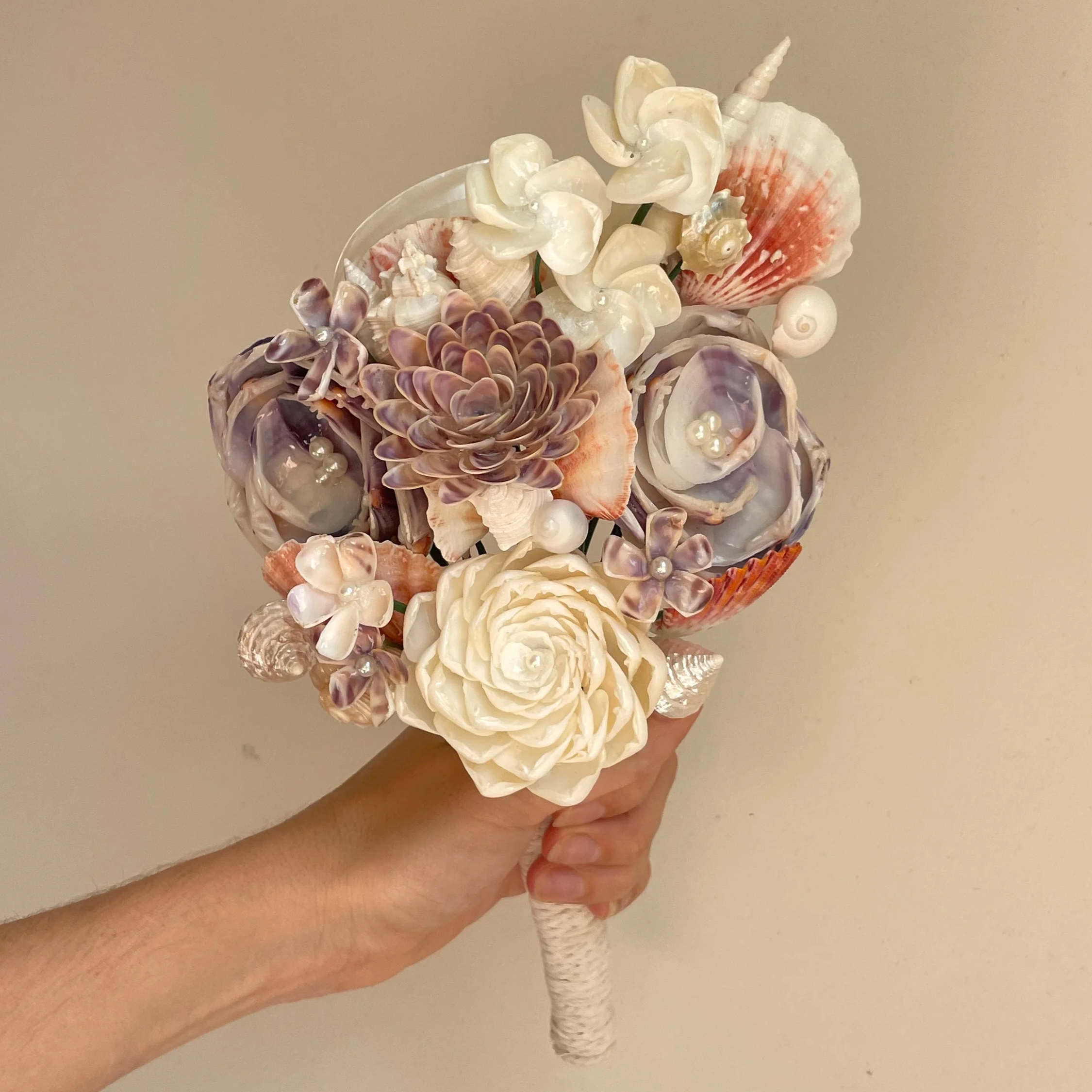 Person holding an ice cream cone decorated with seashells, pearls, and artificial flowers.