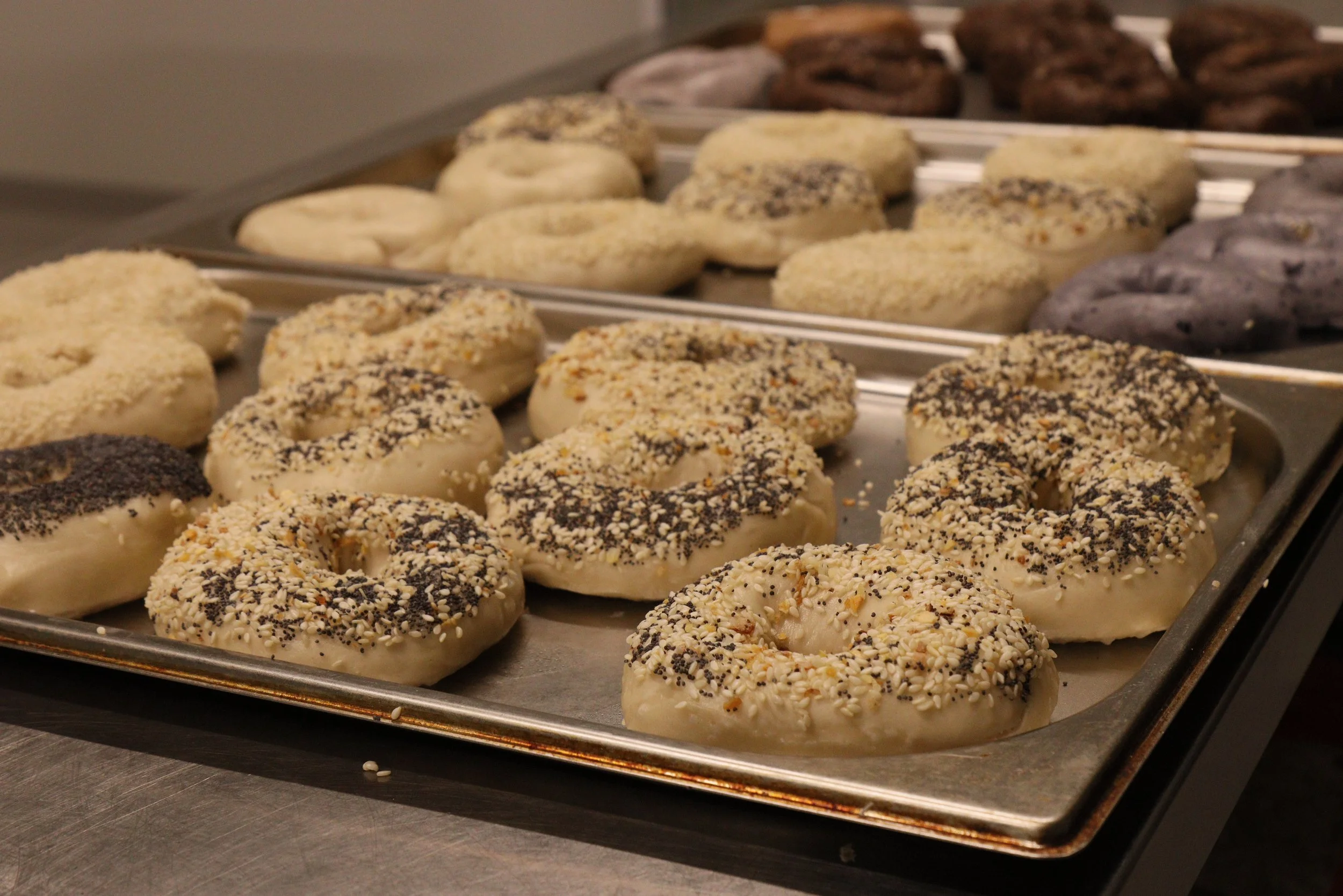Tray of various donuts with different toppings, including sprinkles and nuts, on a metal surface.