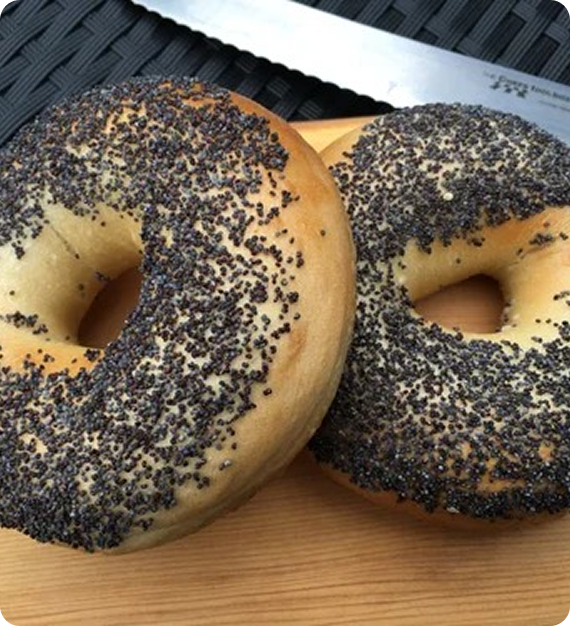 Two bagels topped with poppy seeds on a wooden surface.