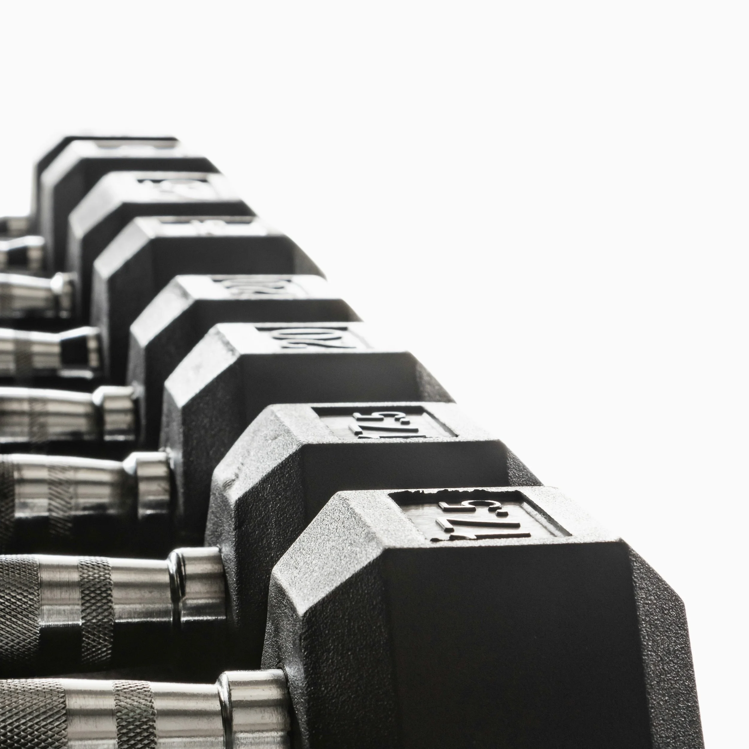 Row of black hex dumbbells used for strength training on a white background.
