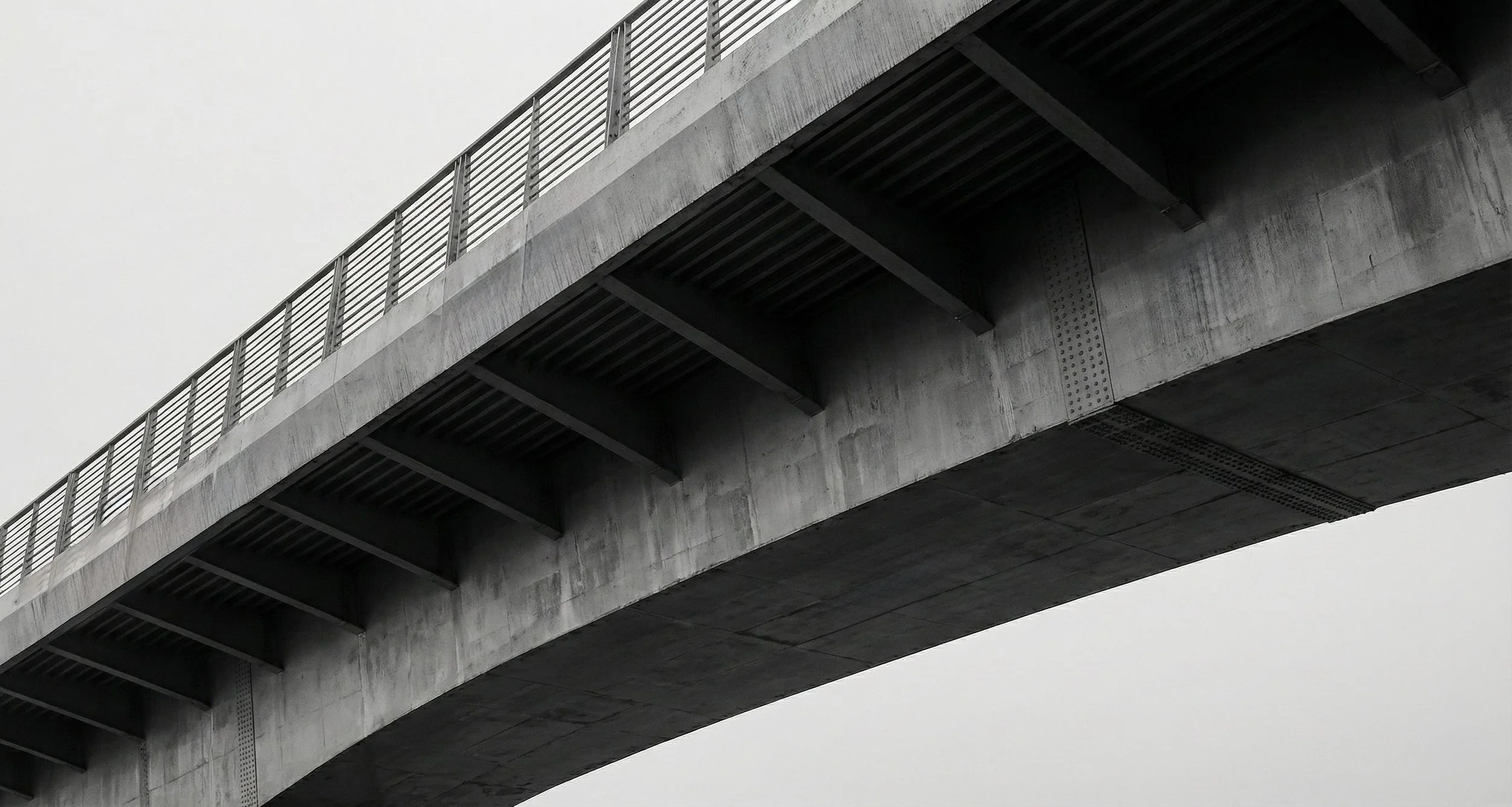 A concrete bridge with metal railings against a cloudy sky.