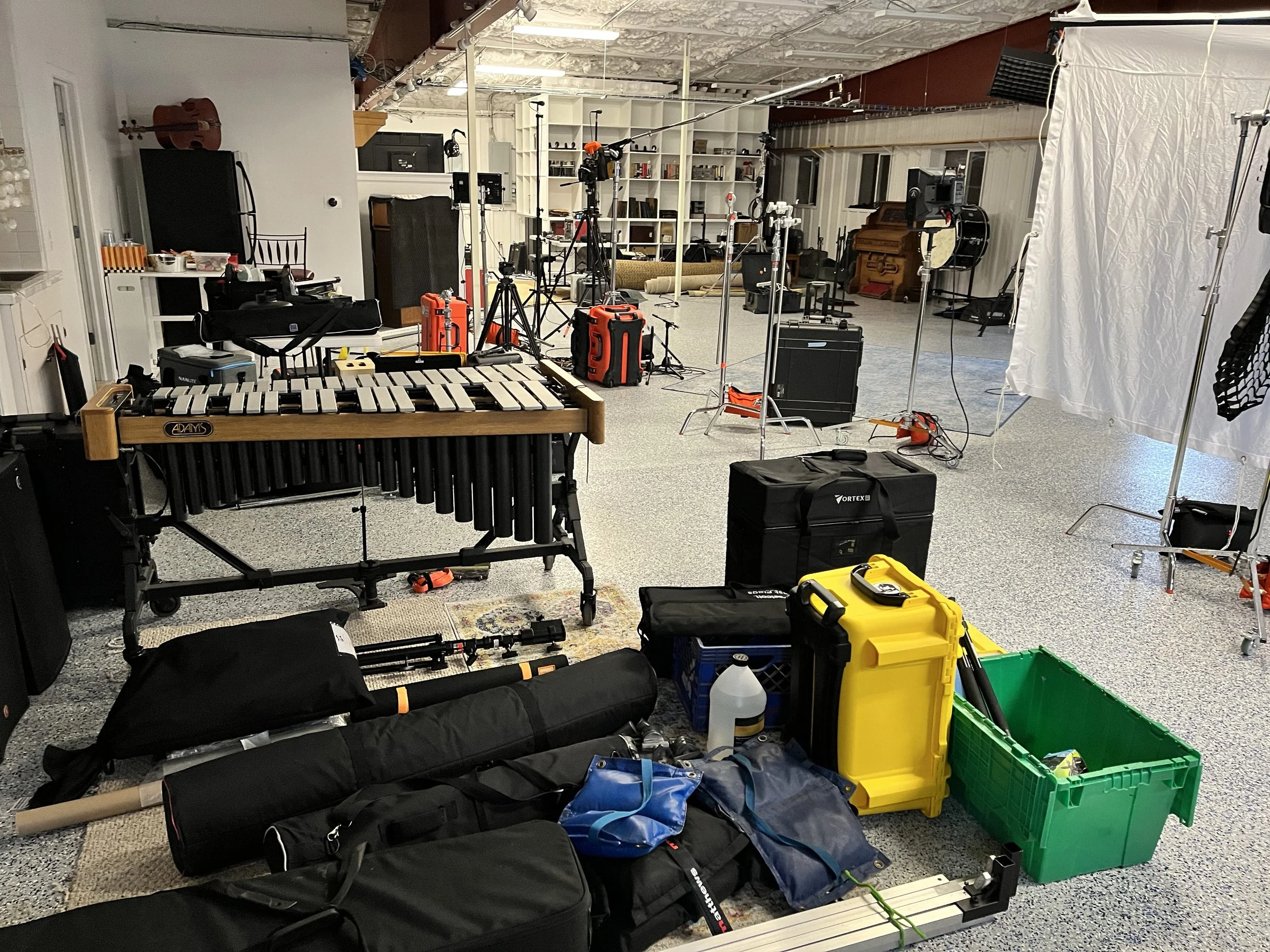 An indoor film or photo shoot studio with various equipment including cameras, lighting, and musical instruments, and a backdrop curtain.