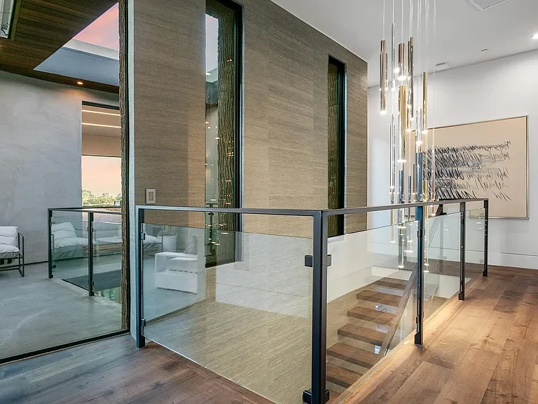 Modern interior with glass railing, wooden staircase, artwork on the wall, and hanging pendant lights.