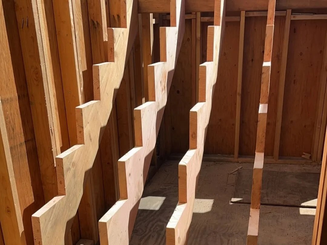 Wooden framework of an unfinished structure with vertical and horizontal beams casting shadows.