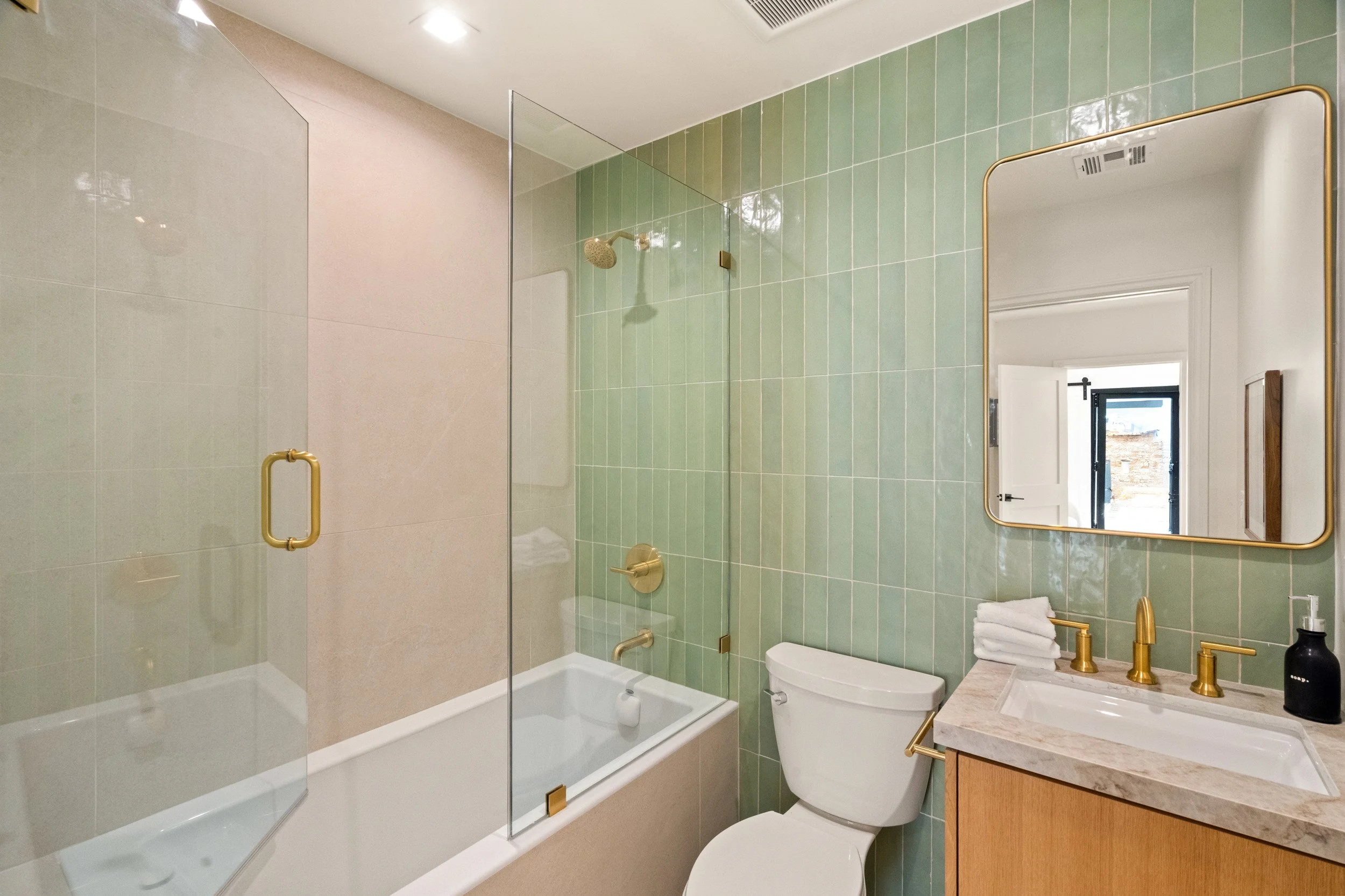 Bathroom with green tile, glass tub screen, and wood vanity.