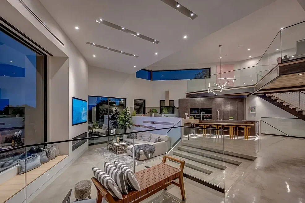 Modern open-concept living room with a staircase, large windows, and contemporary furniture.