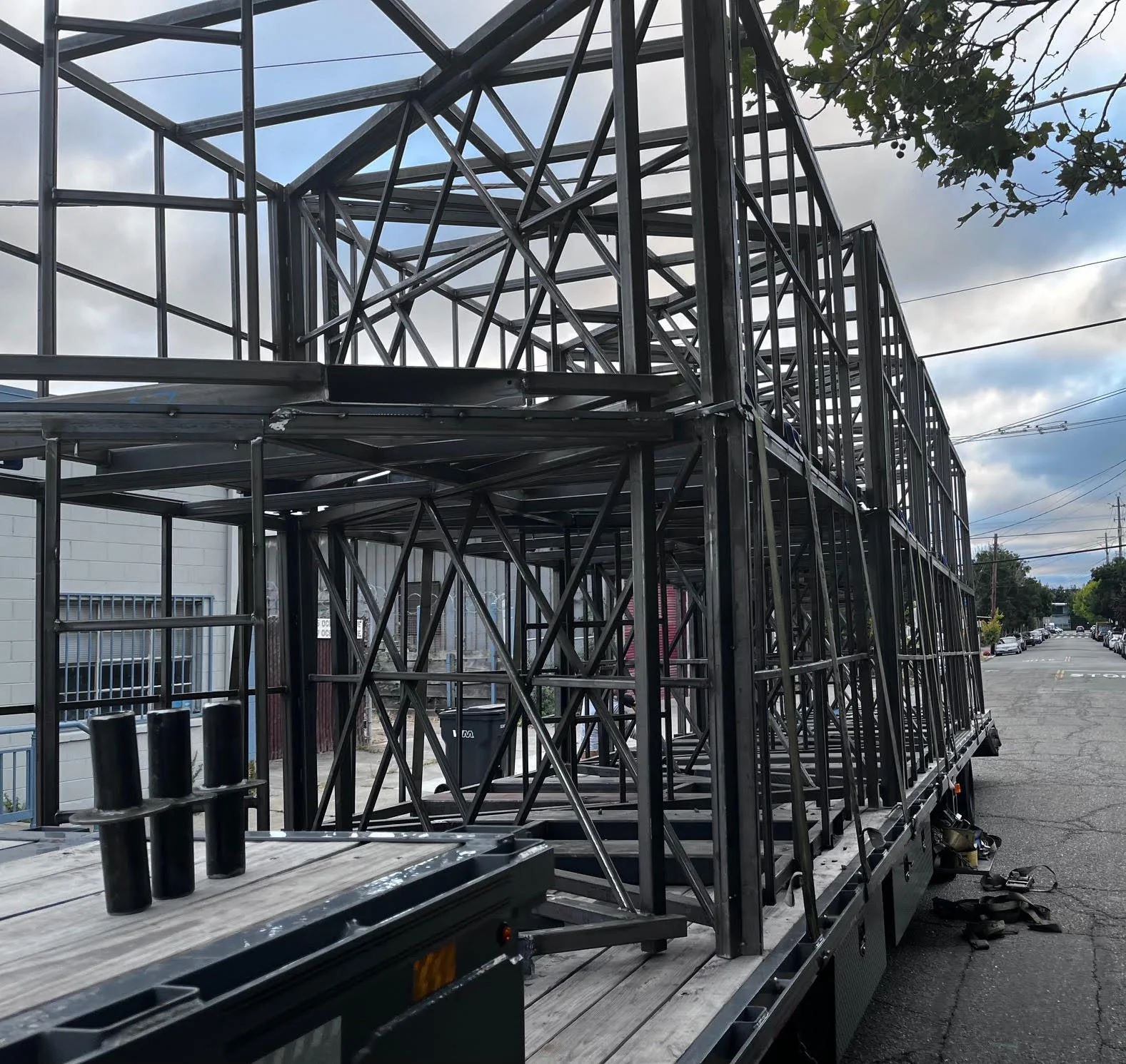 Metal framework structure on a flatbed truck, with a street and cloudy sky in the background.