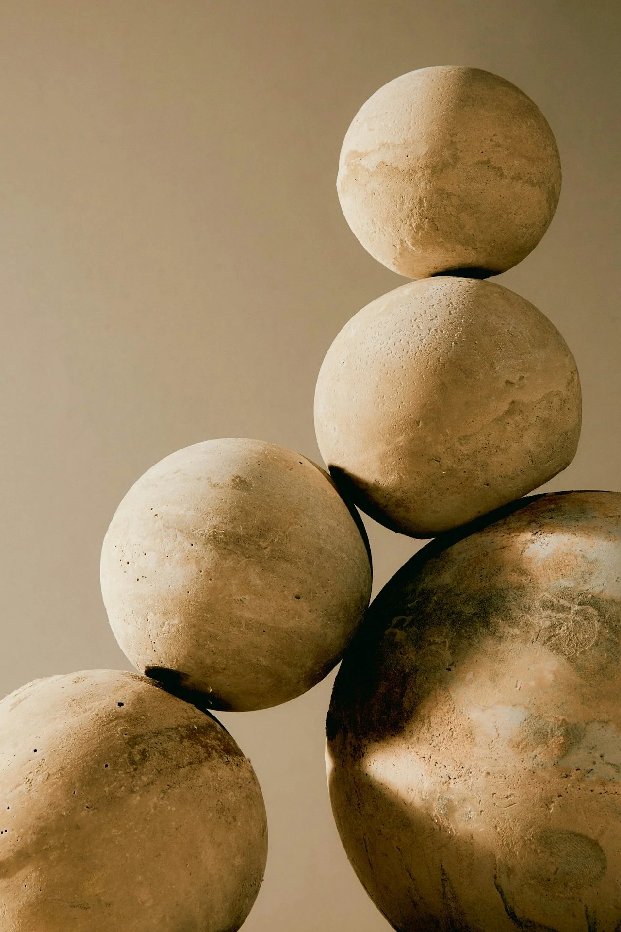 Five round stone balls stacked with three on the bottom and two on top, against a neutral background.