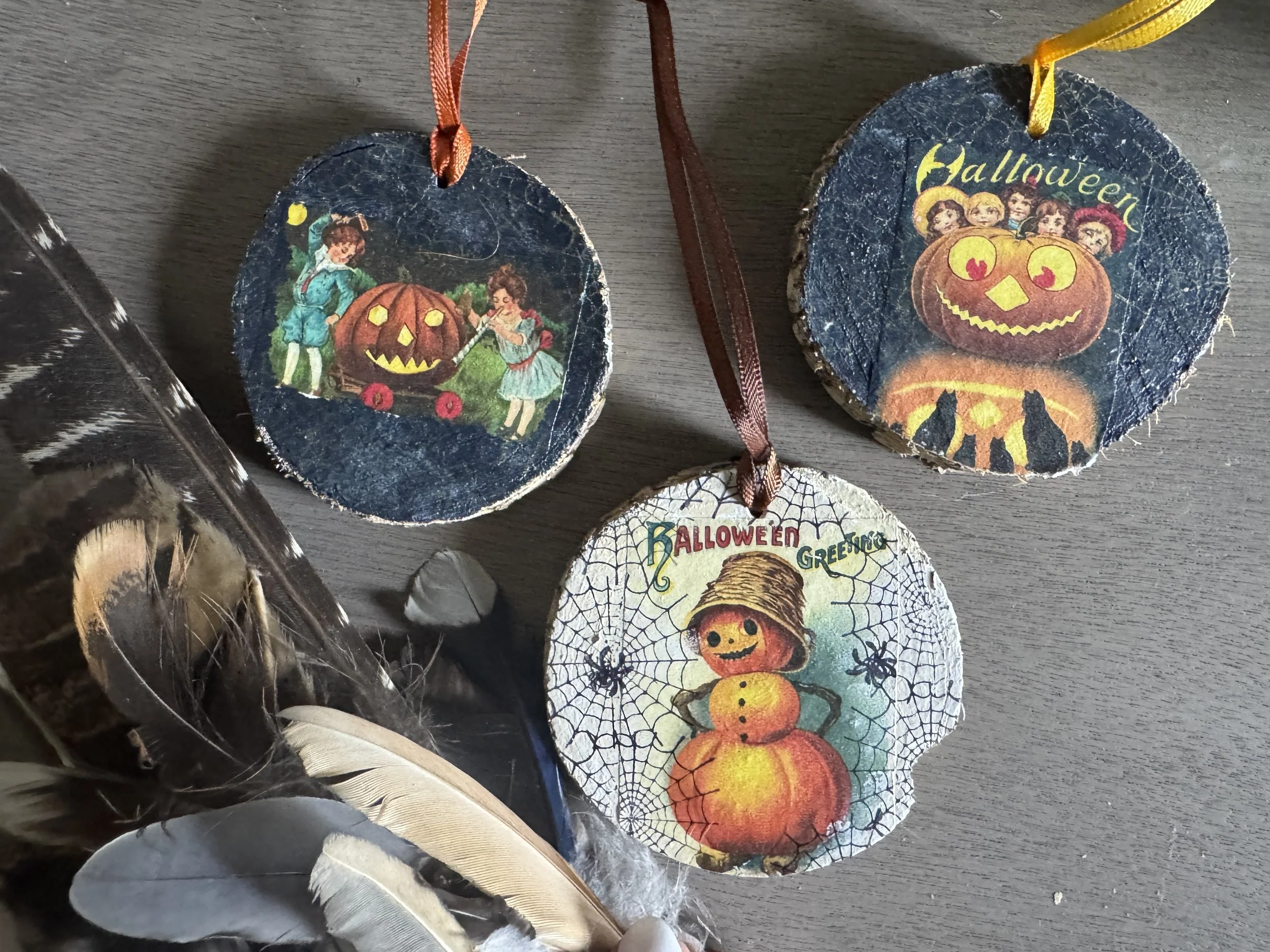 Decorative Halloween ornaments with vintage-style illustrations, including a jack-o'-lantern, children, and a spiderweb design, hanging on ribbons.