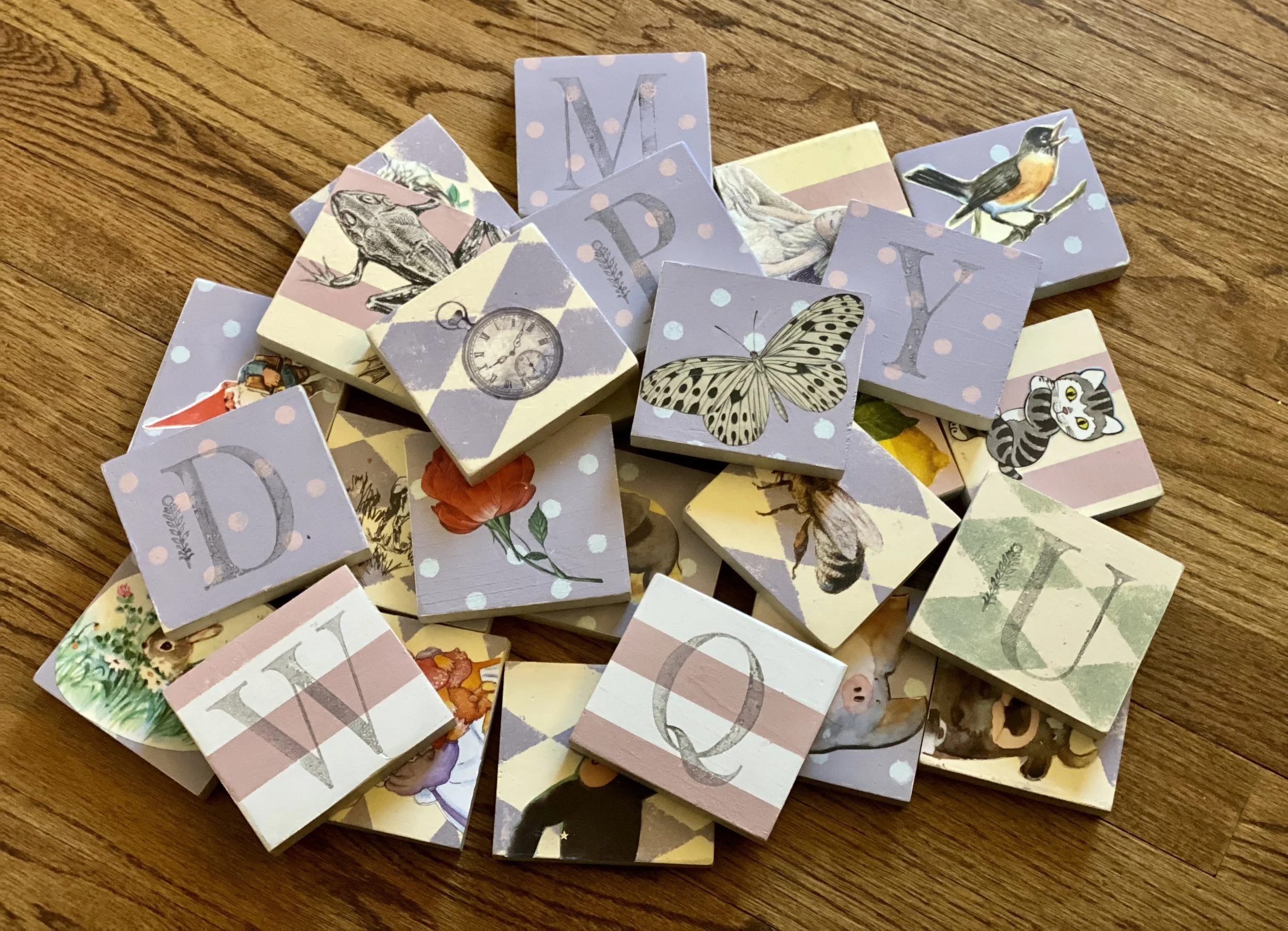 A pile of decorated matchboxes with various illustrations including a butterfly, birds, animals, and numbered letters on a wooden surface.